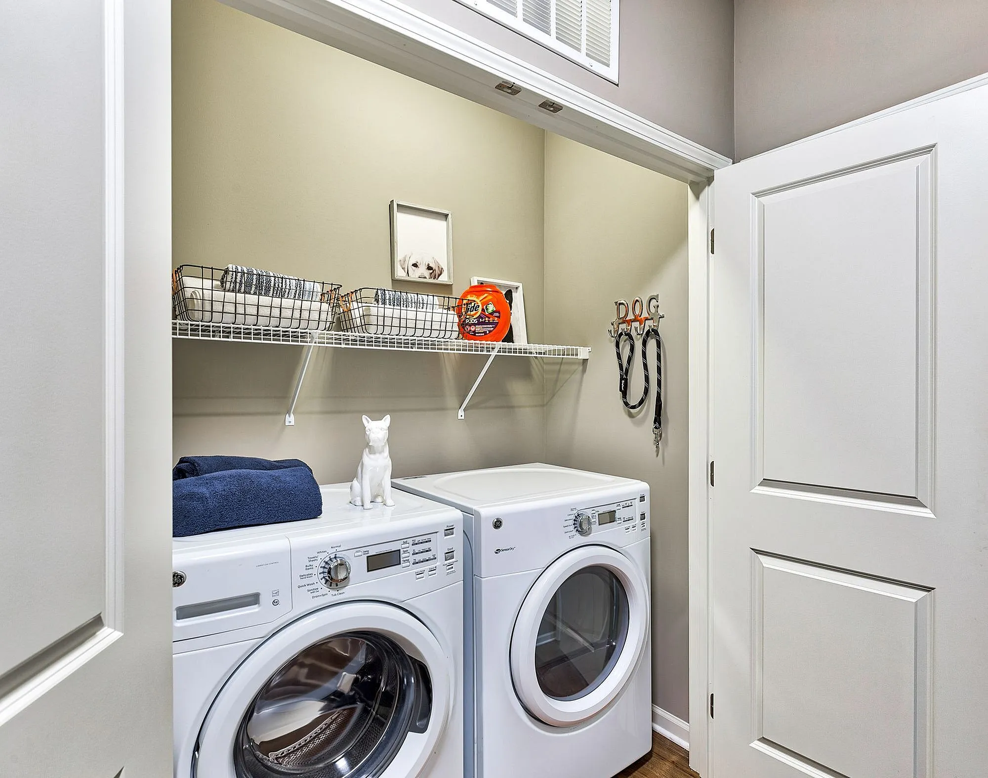Charming laundry closet with modern washer and dryer, featuring elegant shelving for organized storage and delightful pet-themed decor.