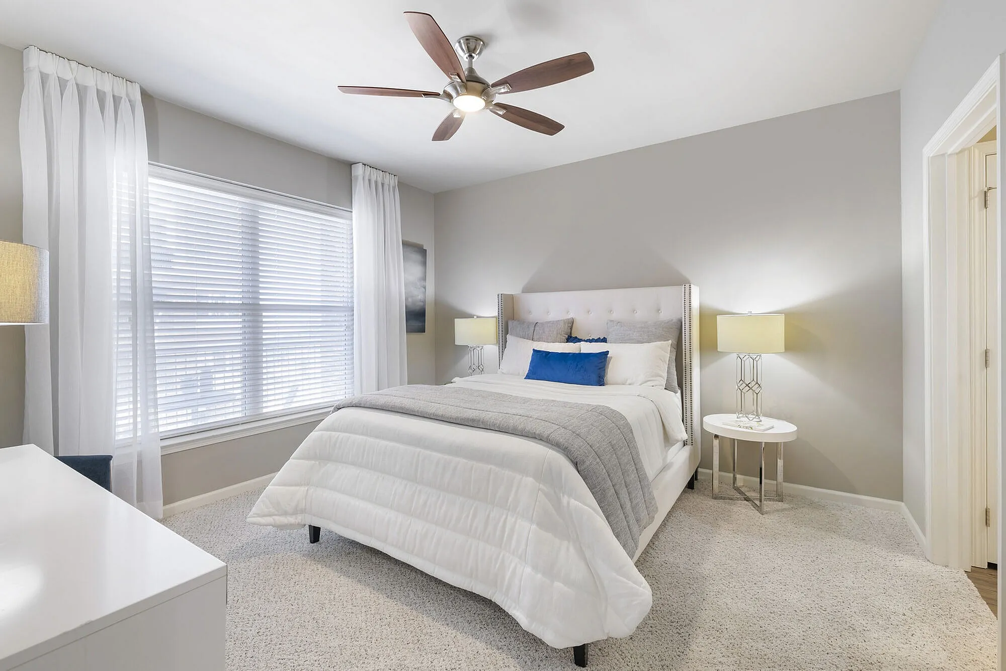 Elegant bedroom featuring a plush bed with stylish cushions, accentuated by soft lighting and a modern ceiling fan, creating a warm and inviting atmosphere.