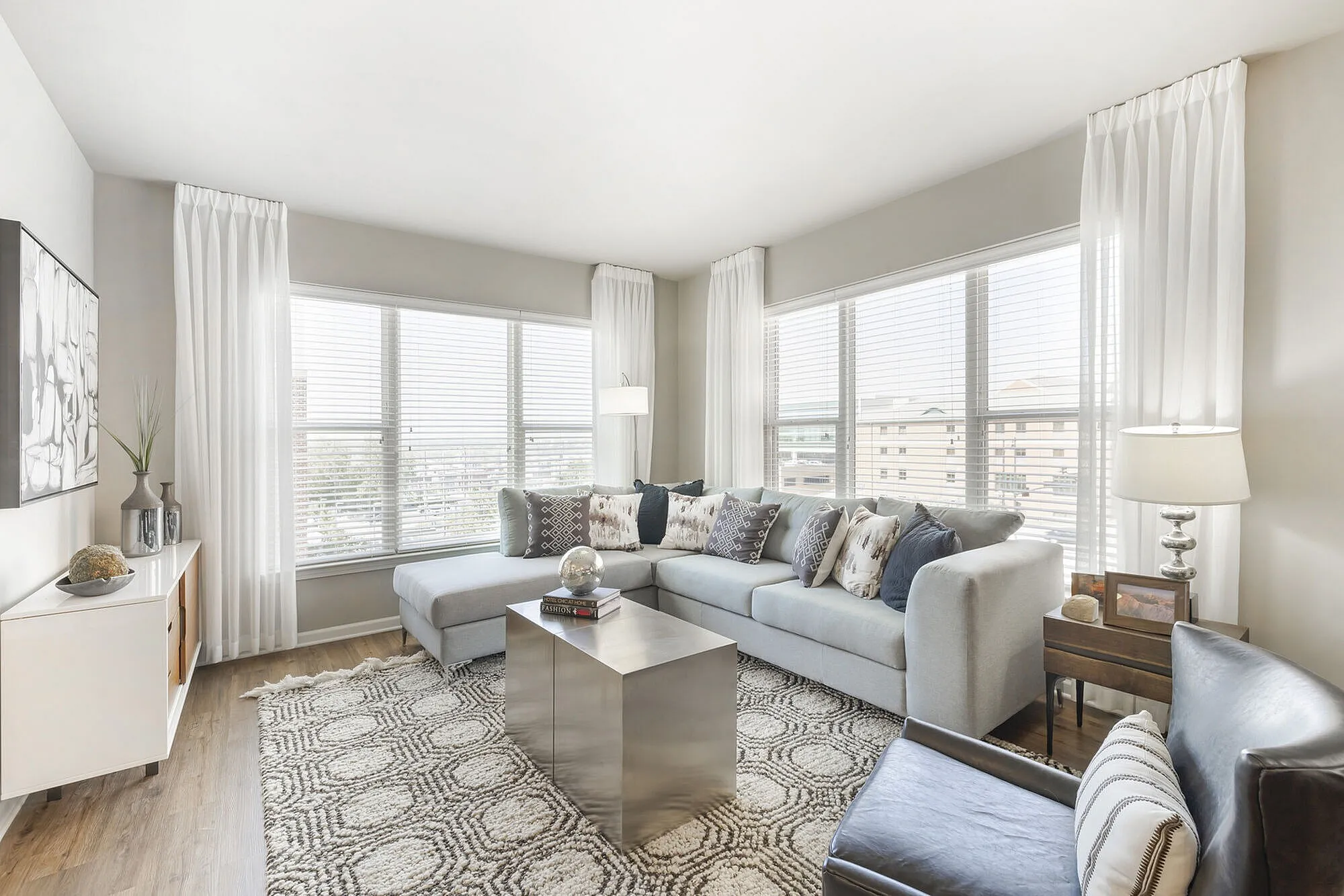 Bright and elegant living room with large windows, sleek sectional sofa, modern decor, and cozy ambiance.