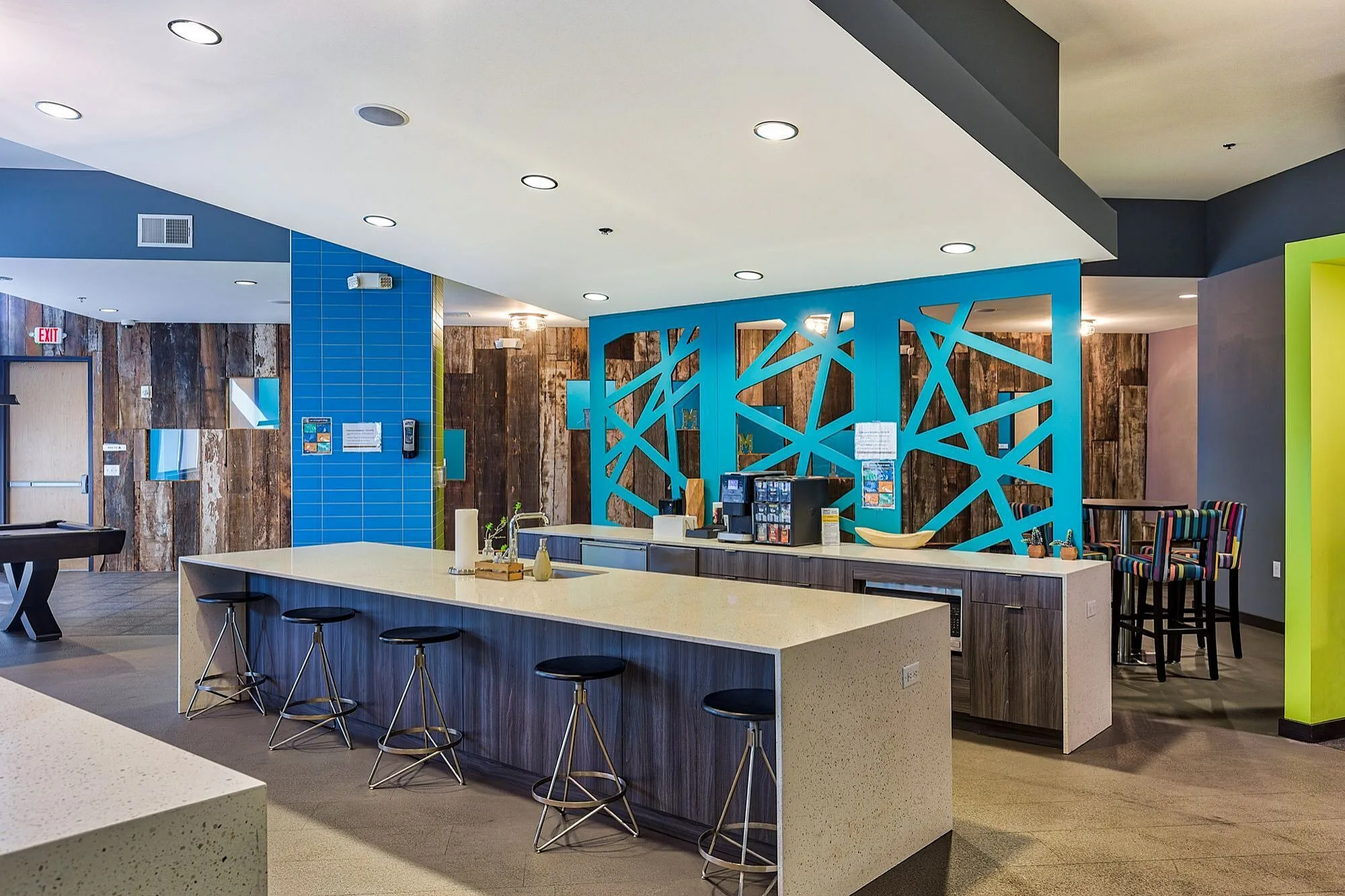 Chic and inviting communal space featuring a modern bar with sleek stools, vibrant blue accent walls, and stylish decor.
