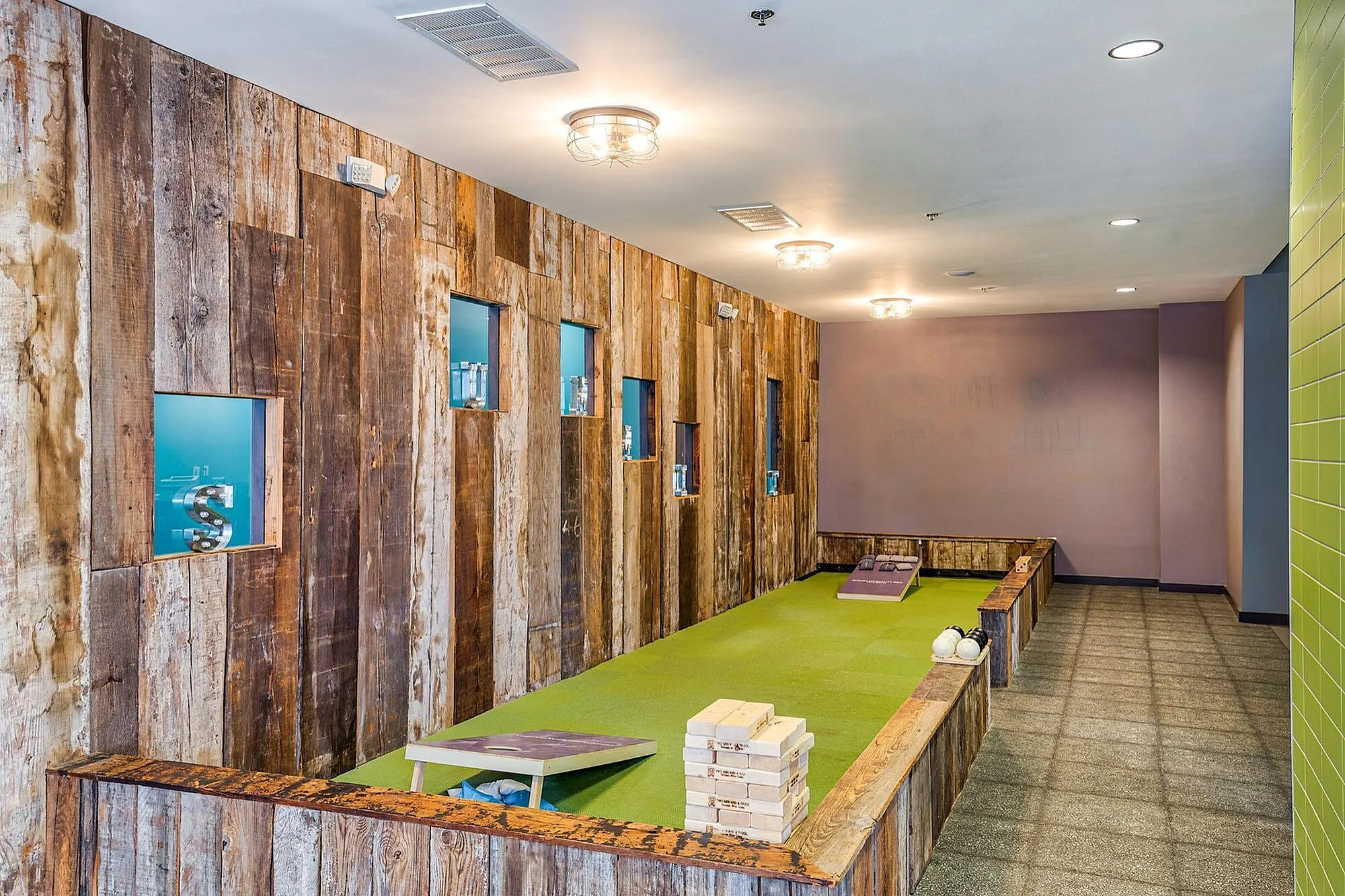 Chic indoor game room showcasing rustic wooden walls, modern light fixtures, and an inviting bocce court with corn hole setup.