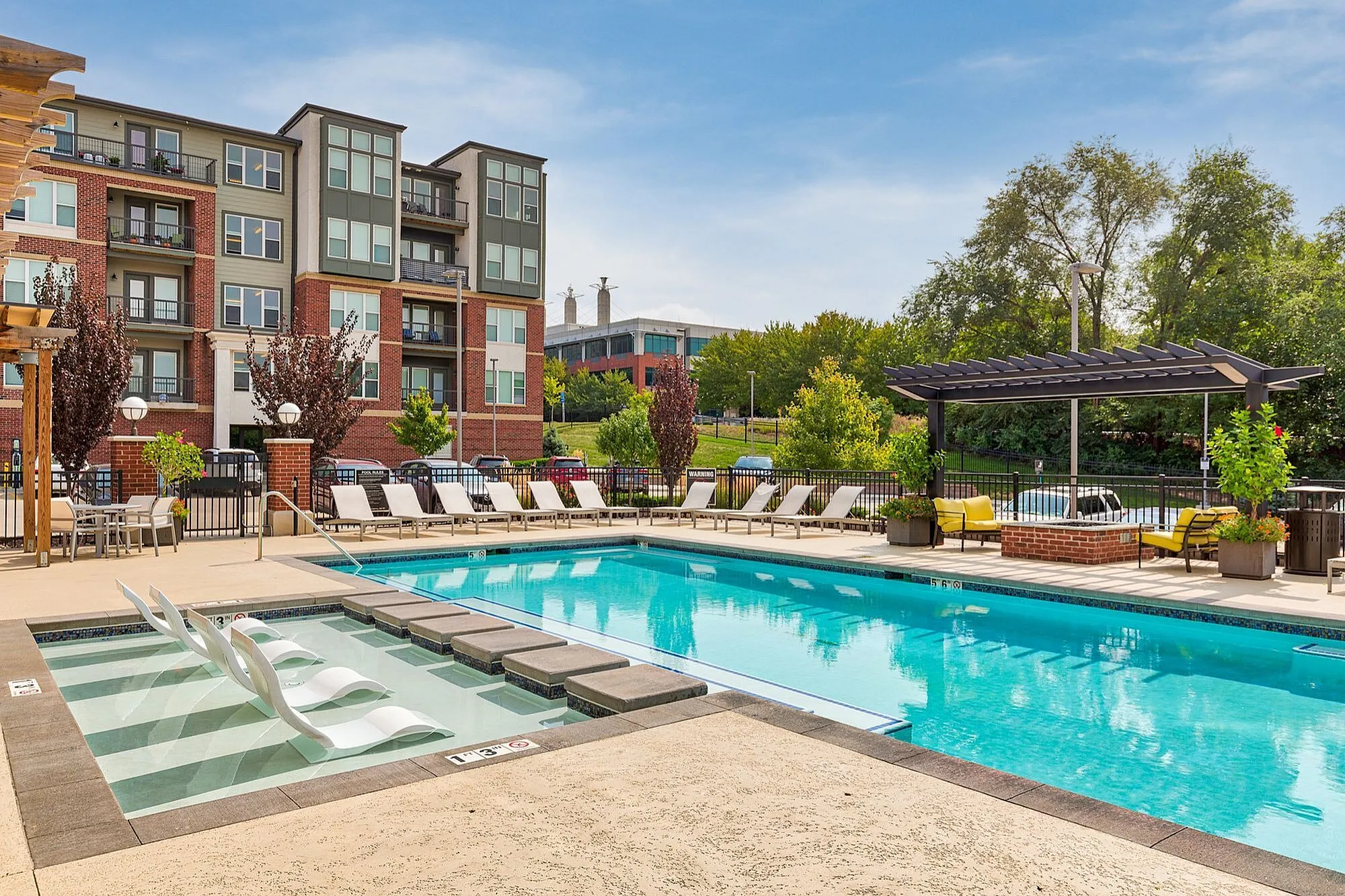 Luxurious apartment complex with a sparkling swimming pool, sun loungers, and lush greenery, offering a resort-style living experience.