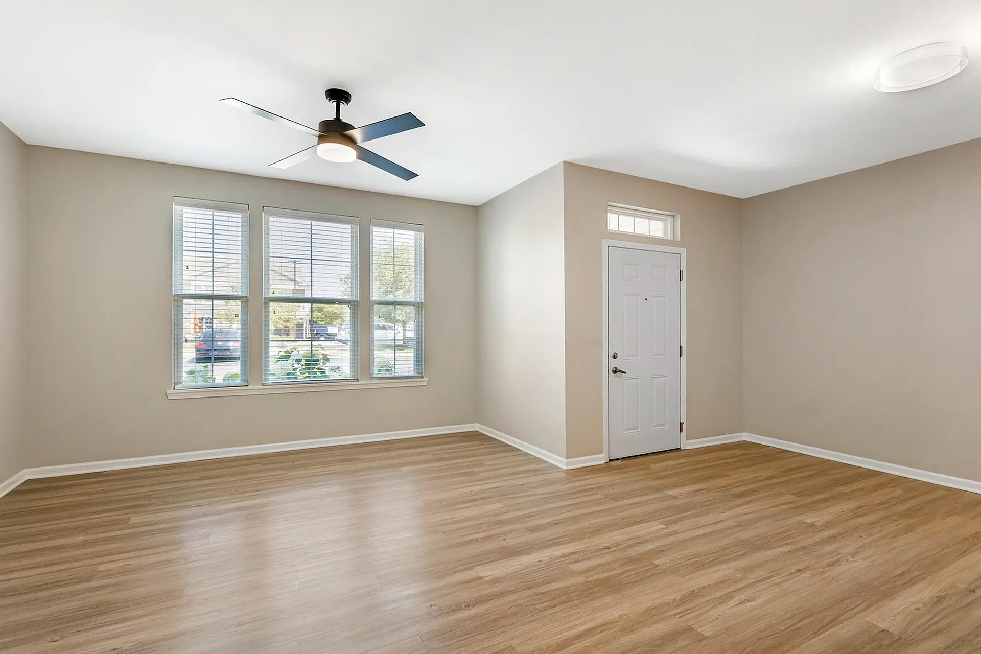 Bright living space with elegant wood flooring, modern ceiling fan, and large windows offering natural light.