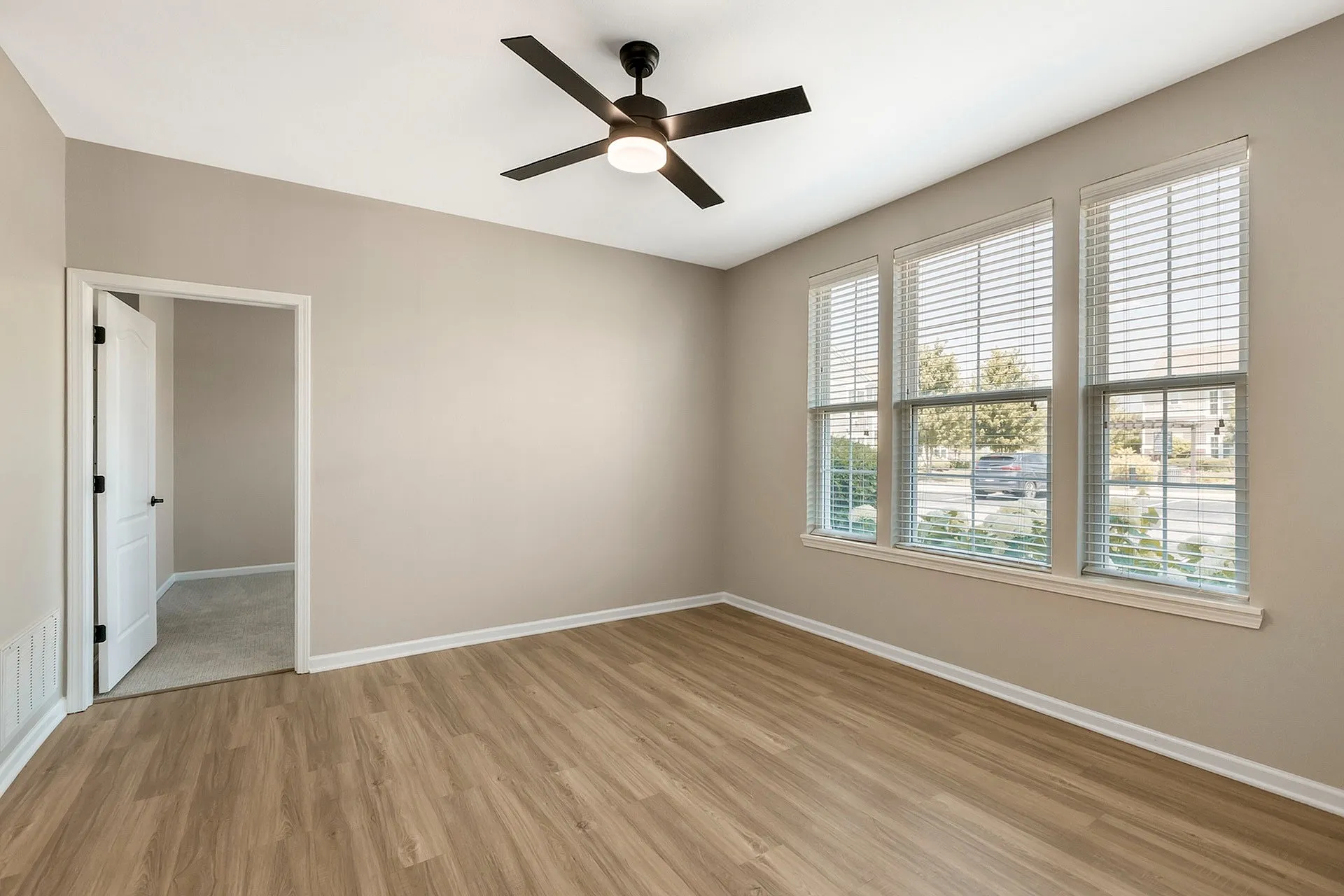 Bright and inviting room with elegant wood flooring, large windows, and a modern ceiling fan, perfect for a cozy living space.