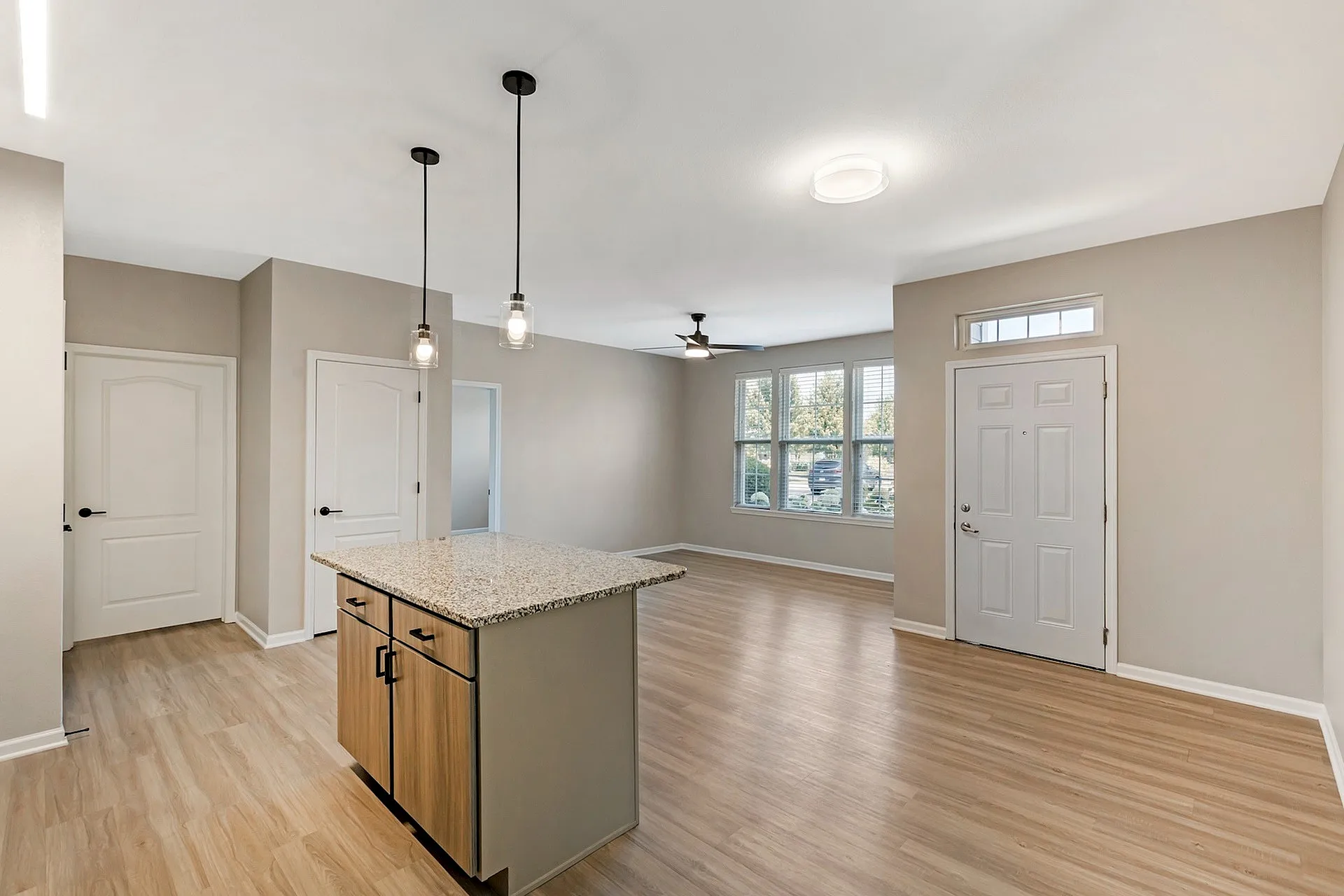 Bright open-concept interior featuring elegant wood flooring, a stylish kitchen island with granite countertop, and abundant natural light through large windows.