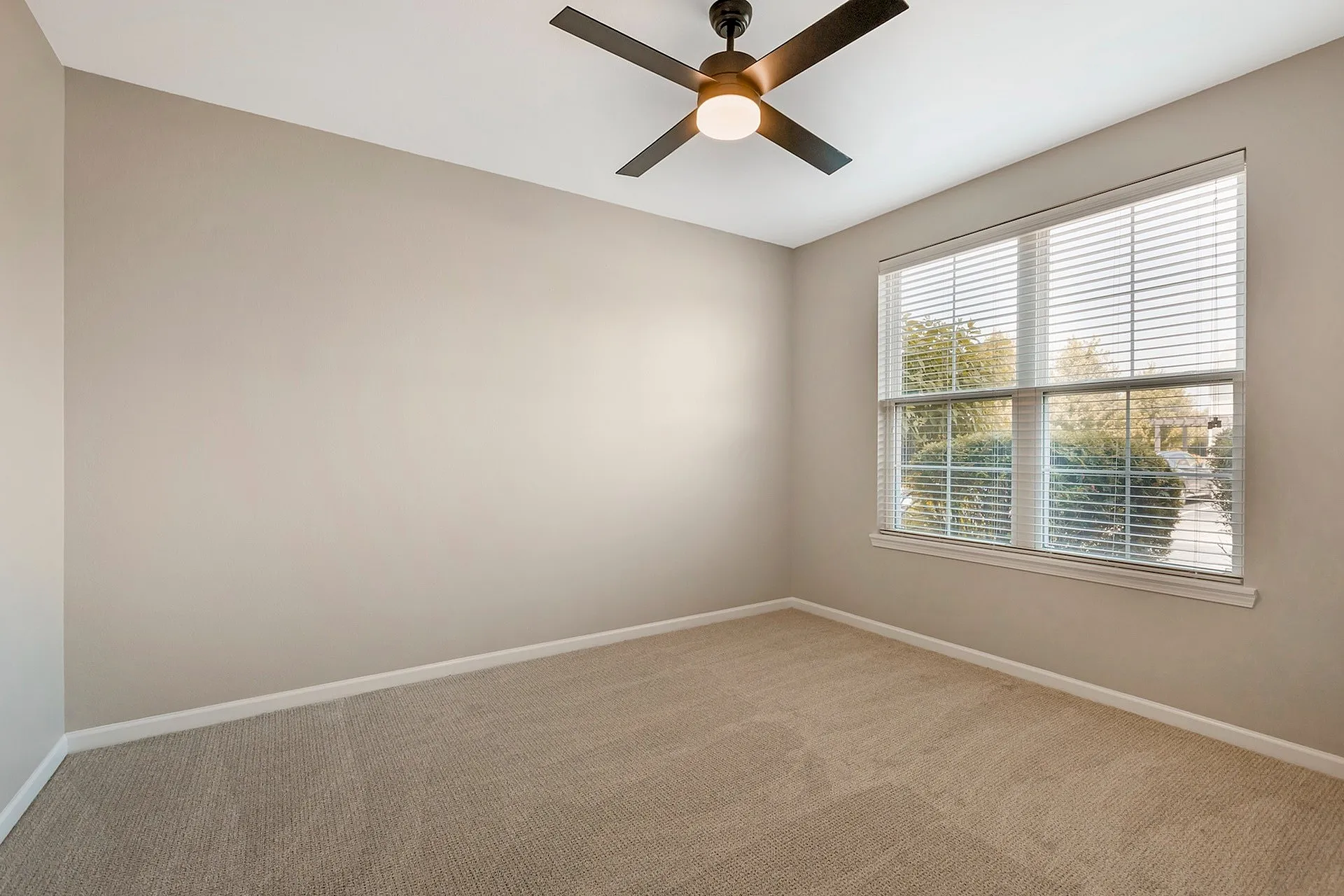 Bright and airy bedroom with neutral tones, a modern ceiling fan, and large window offering natural light and scenic views.