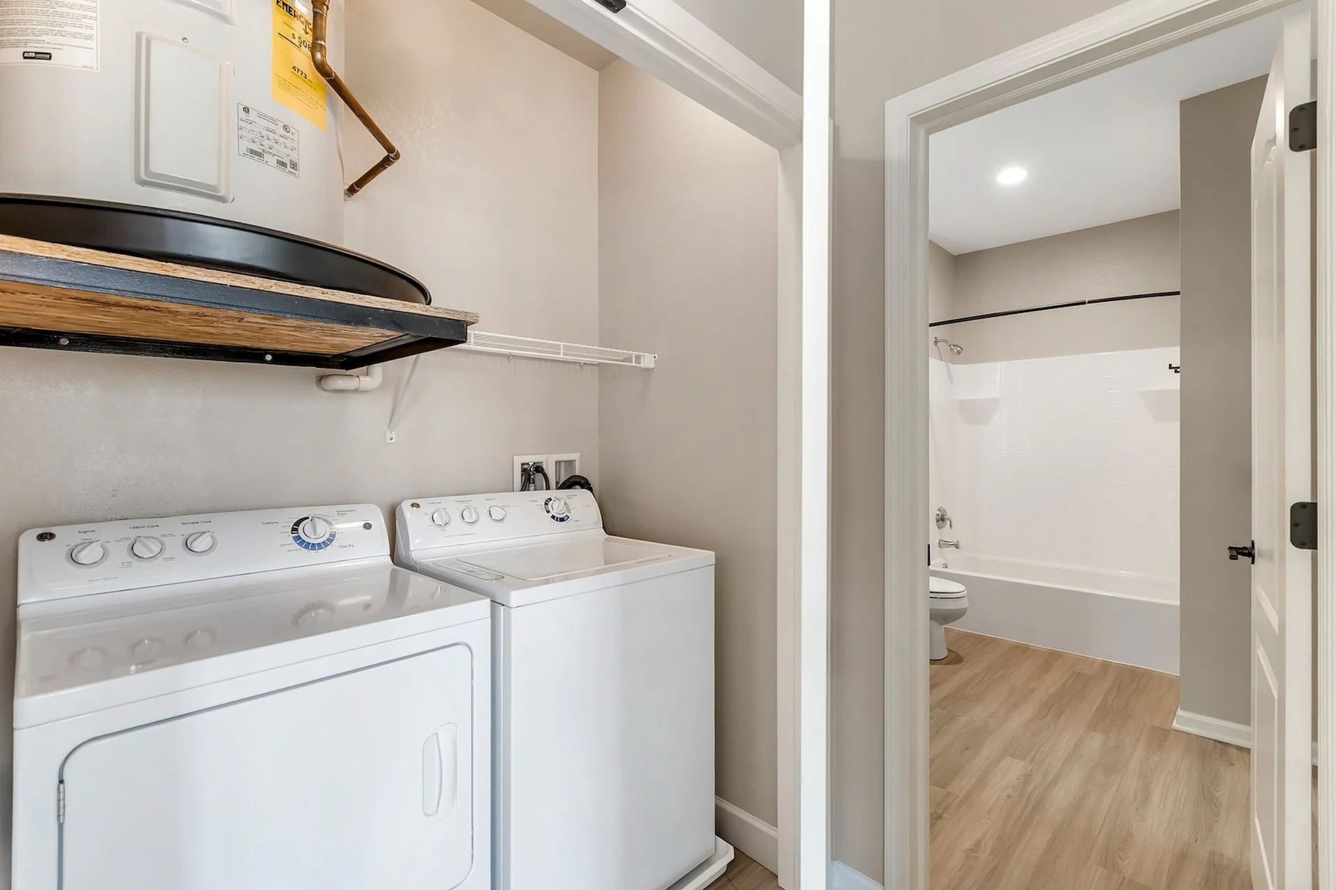 Modern apartment featuring a convenient in-unit laundry area with washer and dryer, complemented by a sleek bathroom entrance with elegant wood flooring.