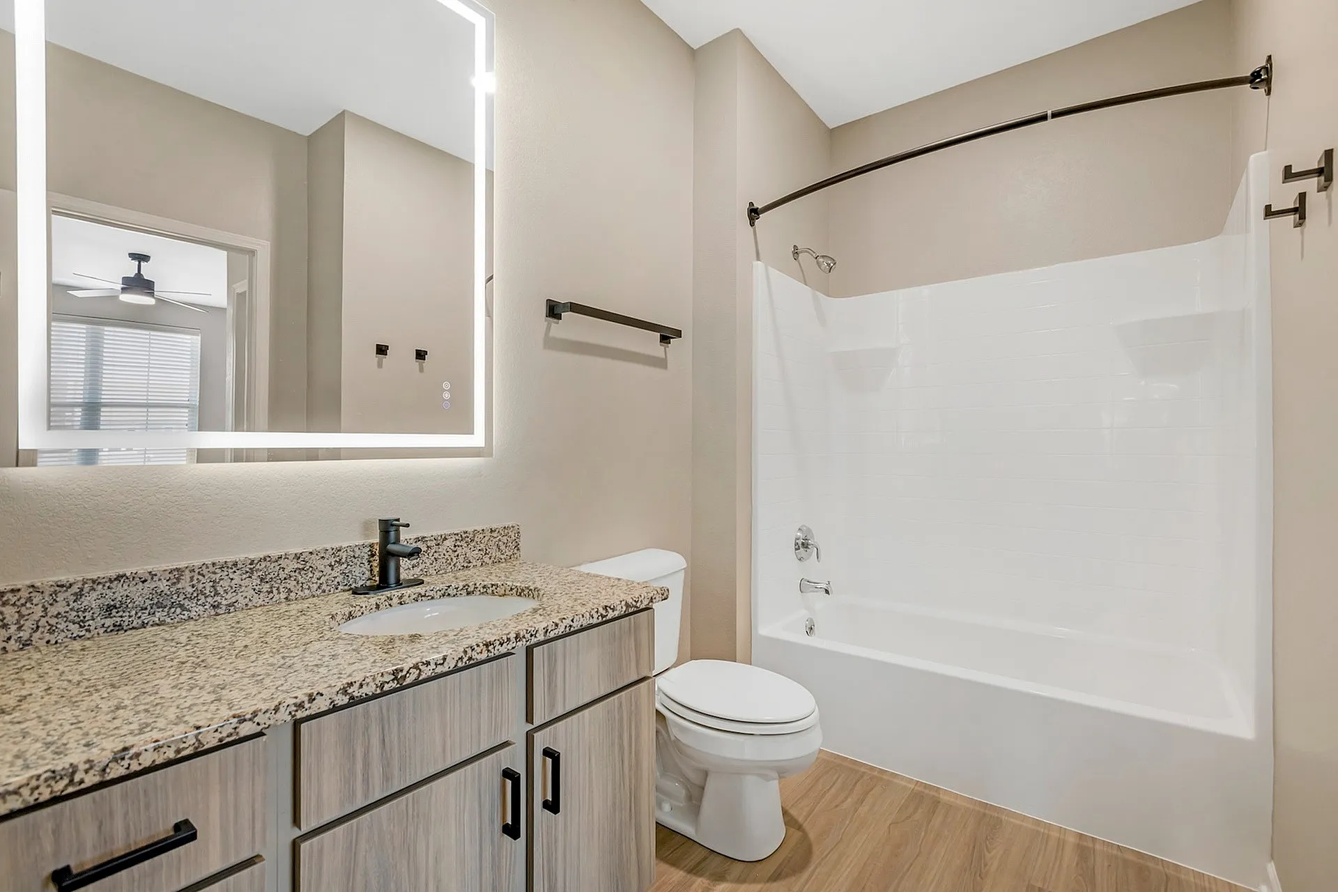 Modern bathroom with granite countertop, sleek fixtures, and a well-lit mirror enhancing elegance.