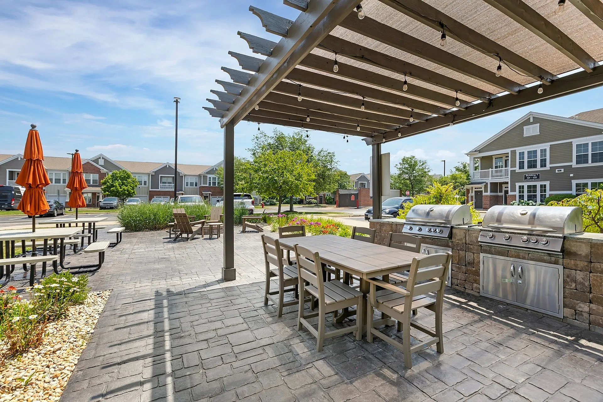 Inviting outdoor patio with grills and seating area under a pergola, perfect for BBQs and social gatherings in a charming community setting.
