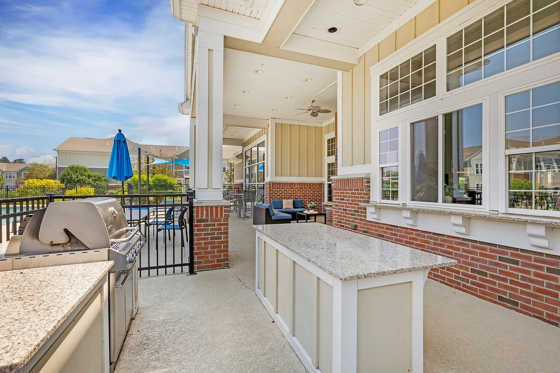 Charming outdoor patio with modern stainless steel grill, comfortable seating, and scenic views under a blue sky.
