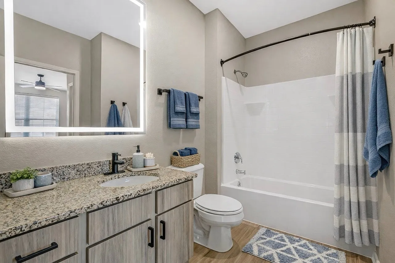 Modern bathroom featuring a sleek vanity with granite countertop, illuminated mirror, and stylish blue accents.