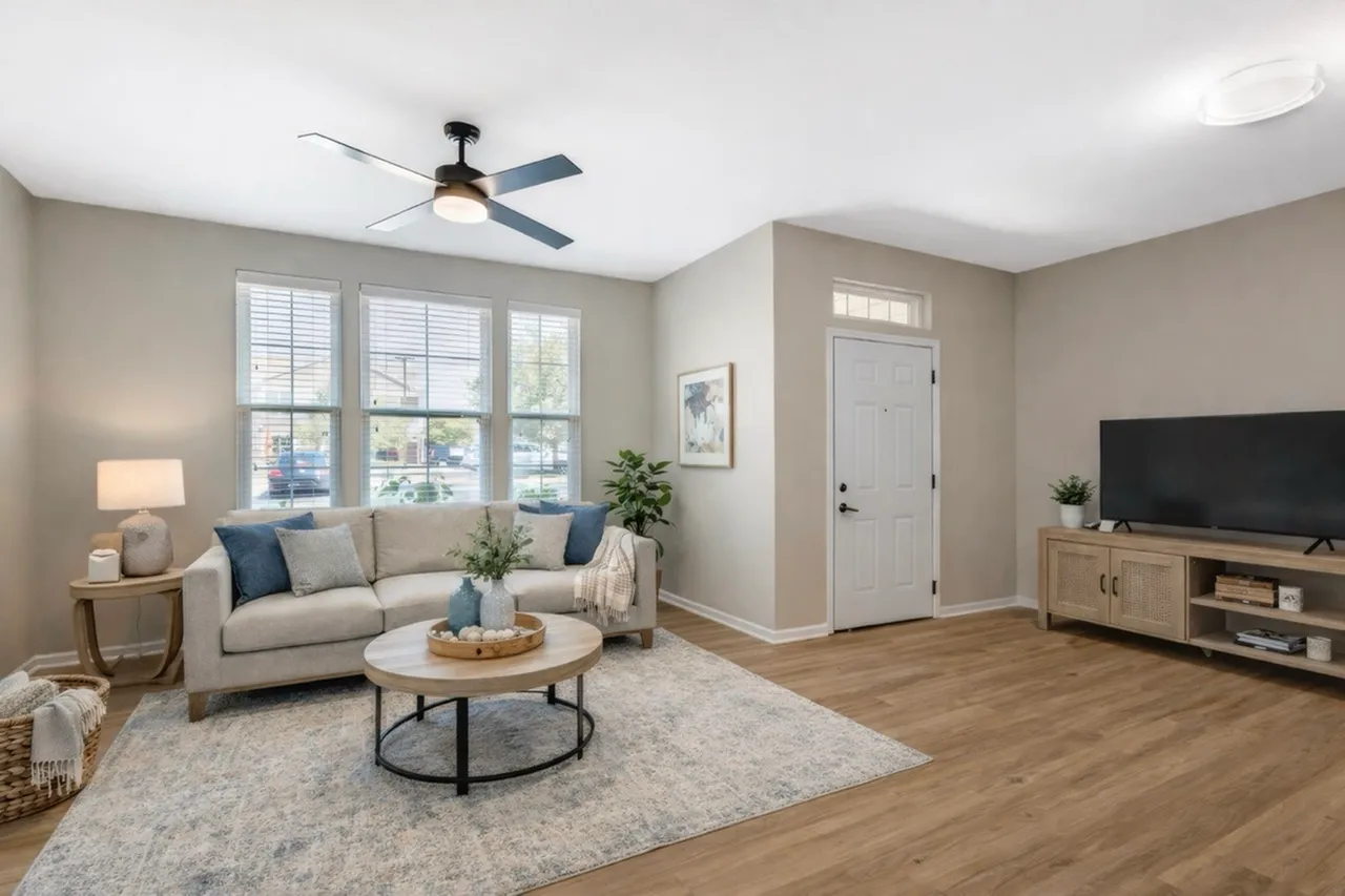 Bright and inviting living room with modern ceiling fan, cozy gray sofa, stylish coffee table, and sleek TV stand on warm hardwood floors.
