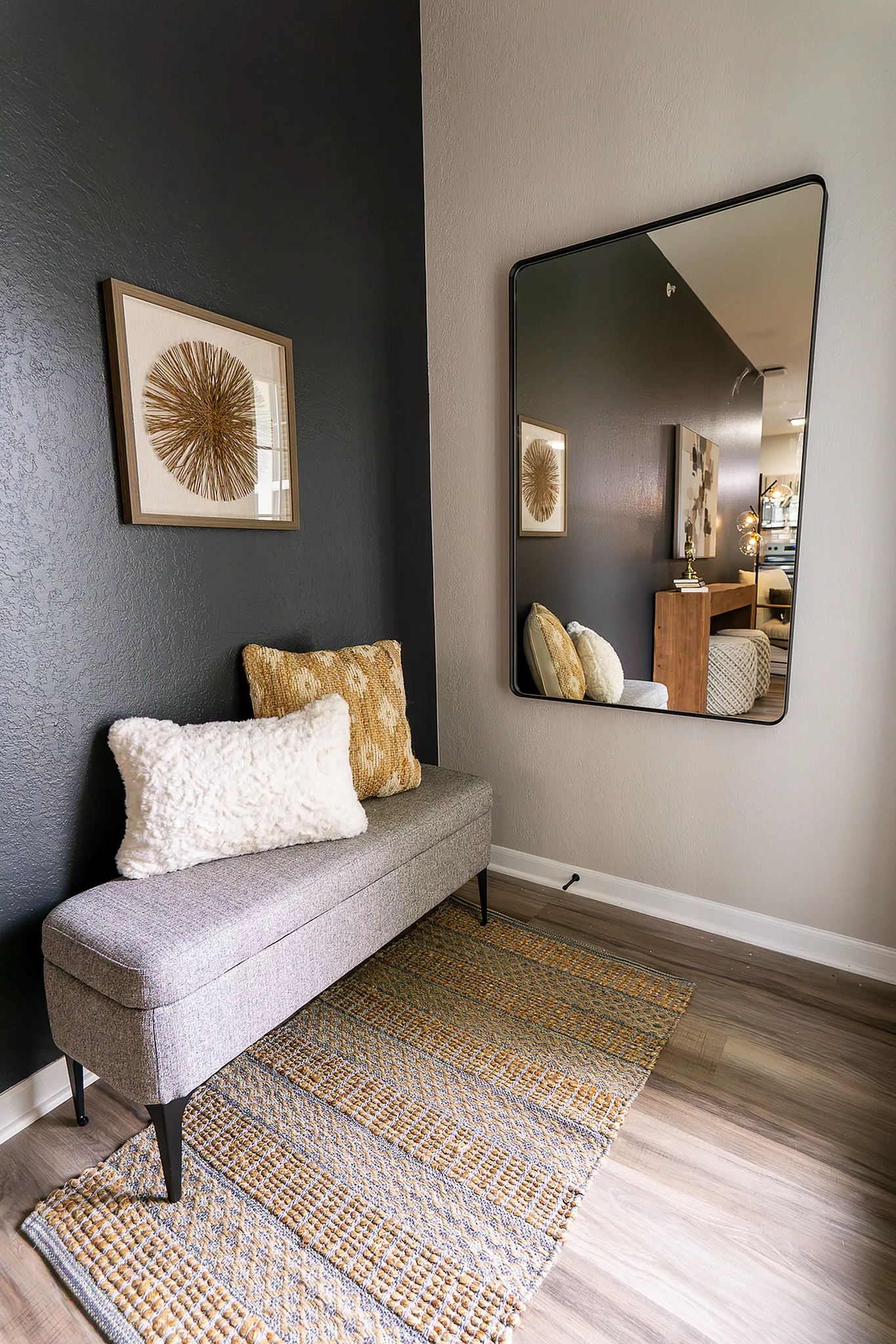 Cozy apartment seating nook with upholstered bench, large mirror and decorative accent wall