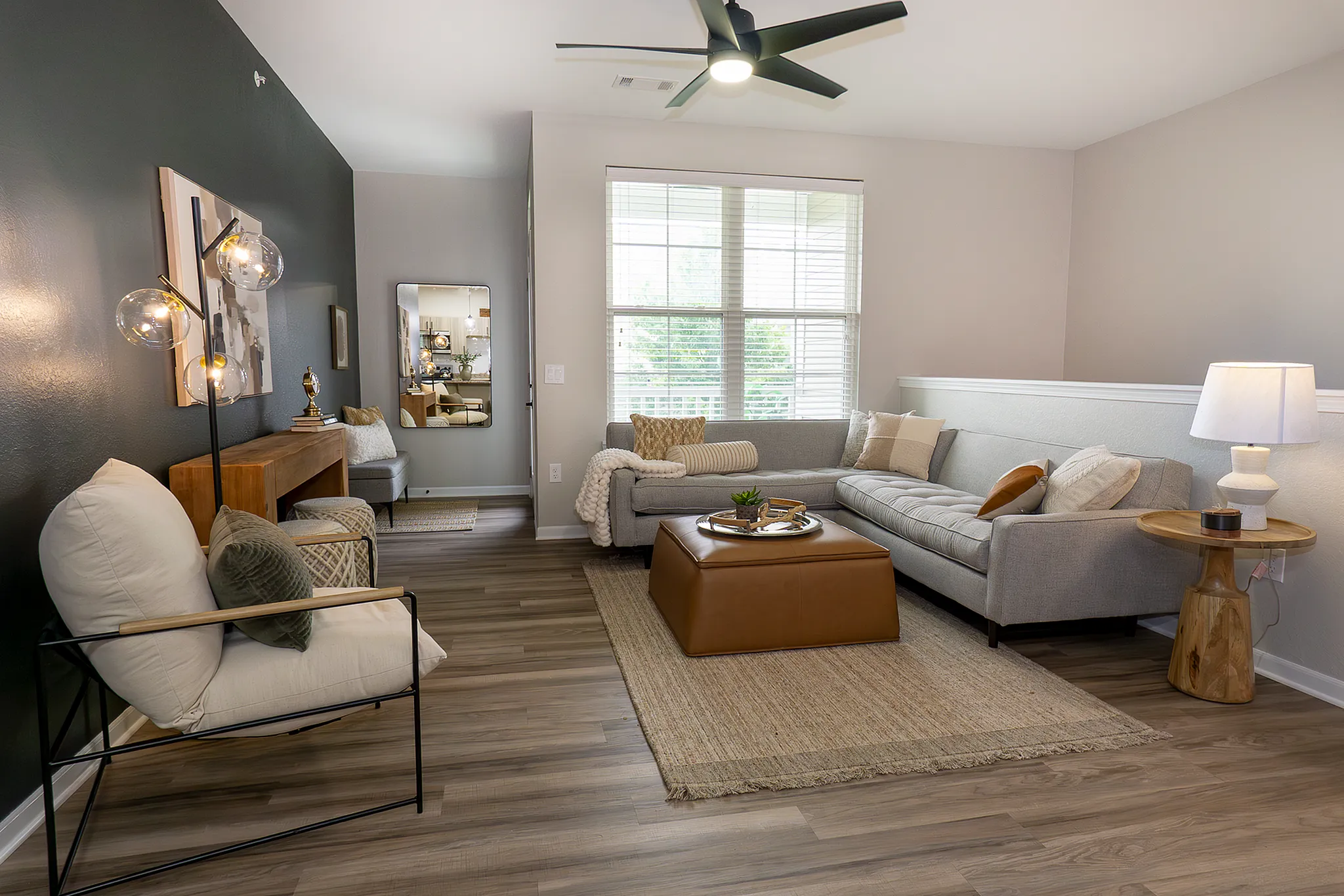 Spacious living room with ceiling fan and sectional seating, natural light from large windows and modern accent wall.