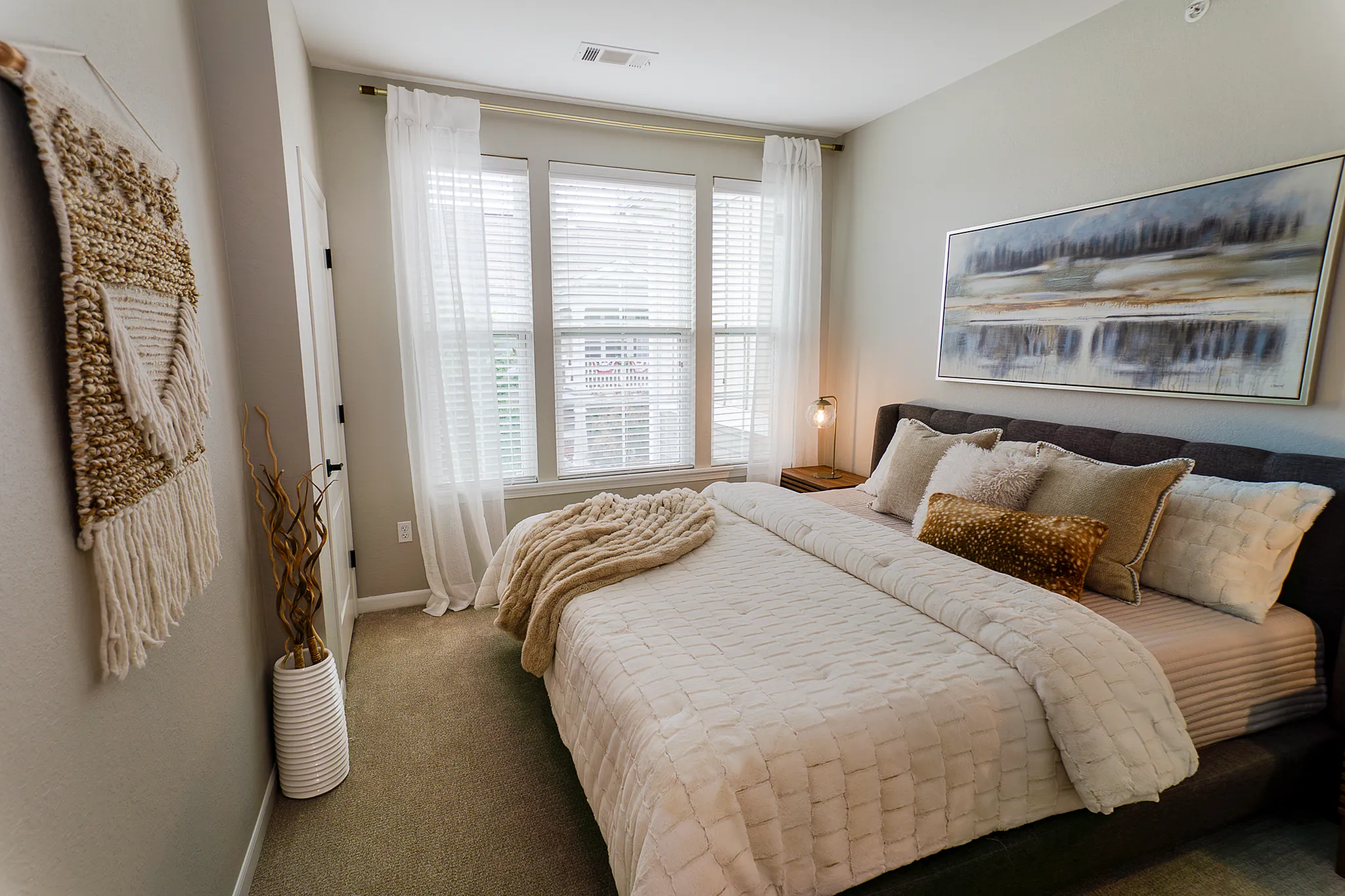 Apartment bedroom with large windows, neutral finishes and a modern upholstered bed.