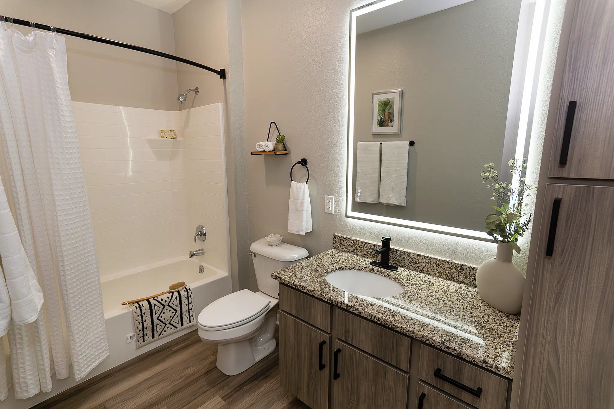 Renovated, spacious apartment bathroom featuring granite vanity, illuminated mirror, and a versatile shower and bathtub combination.
