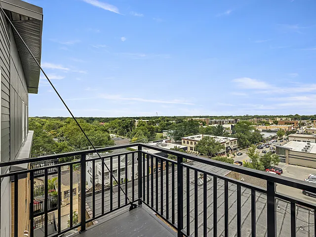 Stunning apartment balcony view overlooking a vibrant neighborhood and lush greenery under a clear blue sky.