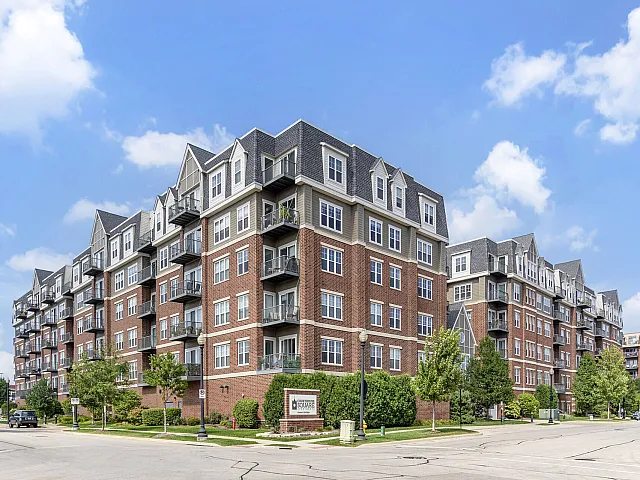 Elegant brick apartment building with modern design, featuring multiple balconies and lush surrounding greenery under a clear blue sky.