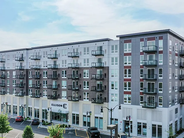 Modern urban apartment building with stylish balconies and vibrant street-level shops, set against a clear blue sky.