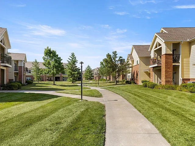 Charming residential pathway surrounded by lush green lawns and modern two-story apartments, offering a serene suburban atmosphere.