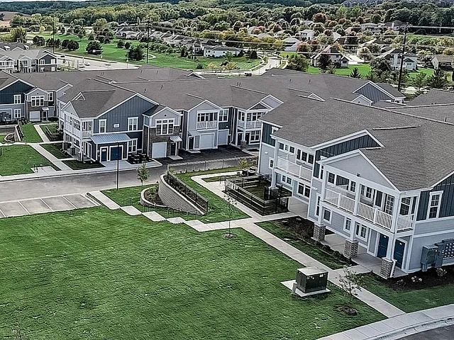 Aerial view of a charming residential neighborhood showcasing modern townhouses, lush green lawns, and scenic countryside surroundings under a vibrant blue sky.