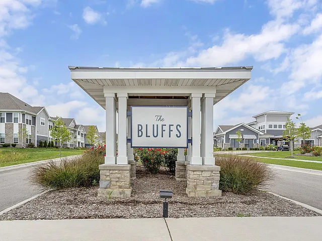 Charming community entrance of The Bluffs with well-maintained landscaping and modern residential buildings under a clear blue sky.