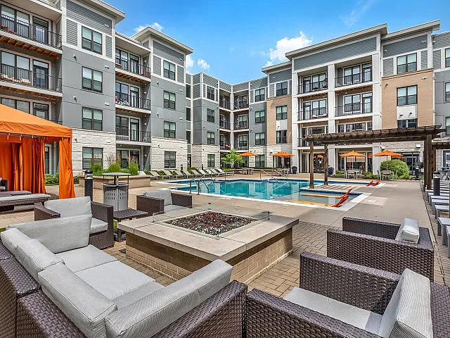 Modern apartment complex with a luxurious pool, stylish cabanas, and comfy lounge areas under clear blue skies.