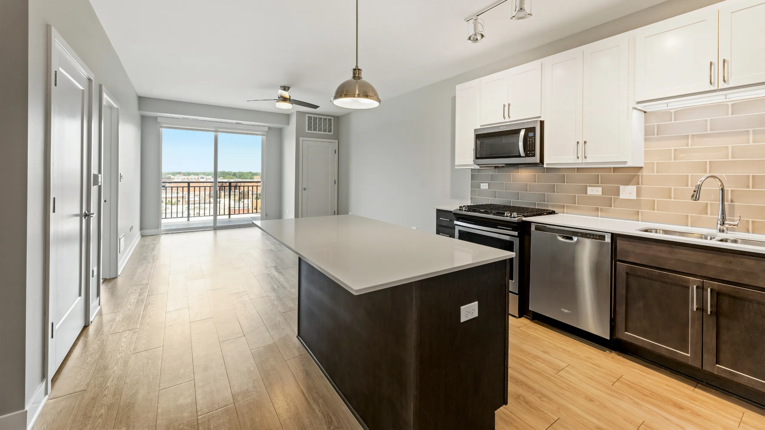 Modern apartment kitchen with an open-concept layout, featuring sleek cabinetry, stainless steel appliances, and an island with a view through large sliding glass doors.