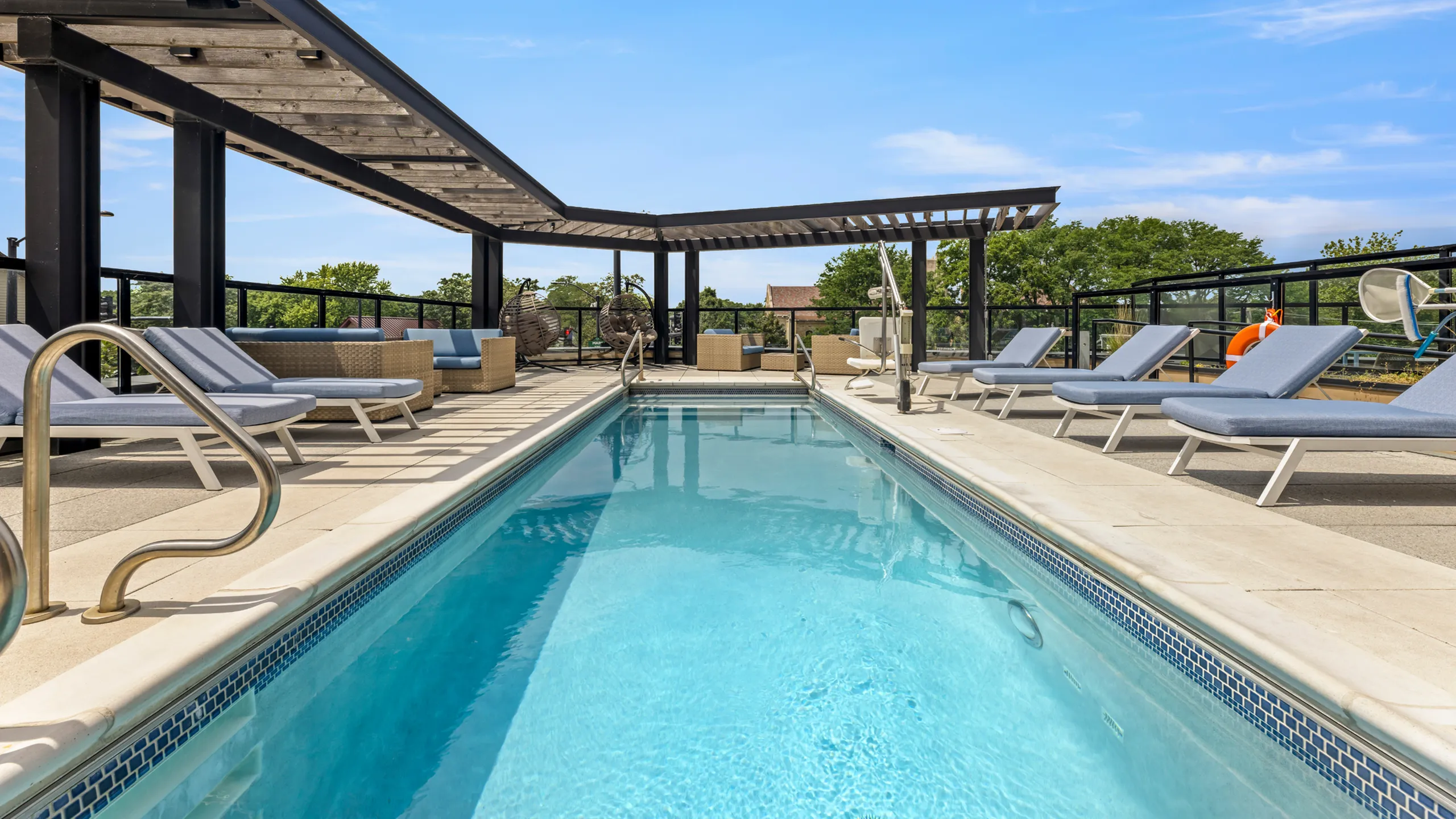 Luxurious rooftop swimming pool with modern lounge chairs and shaded seating, perfect for relaxing under a clear blue sky.