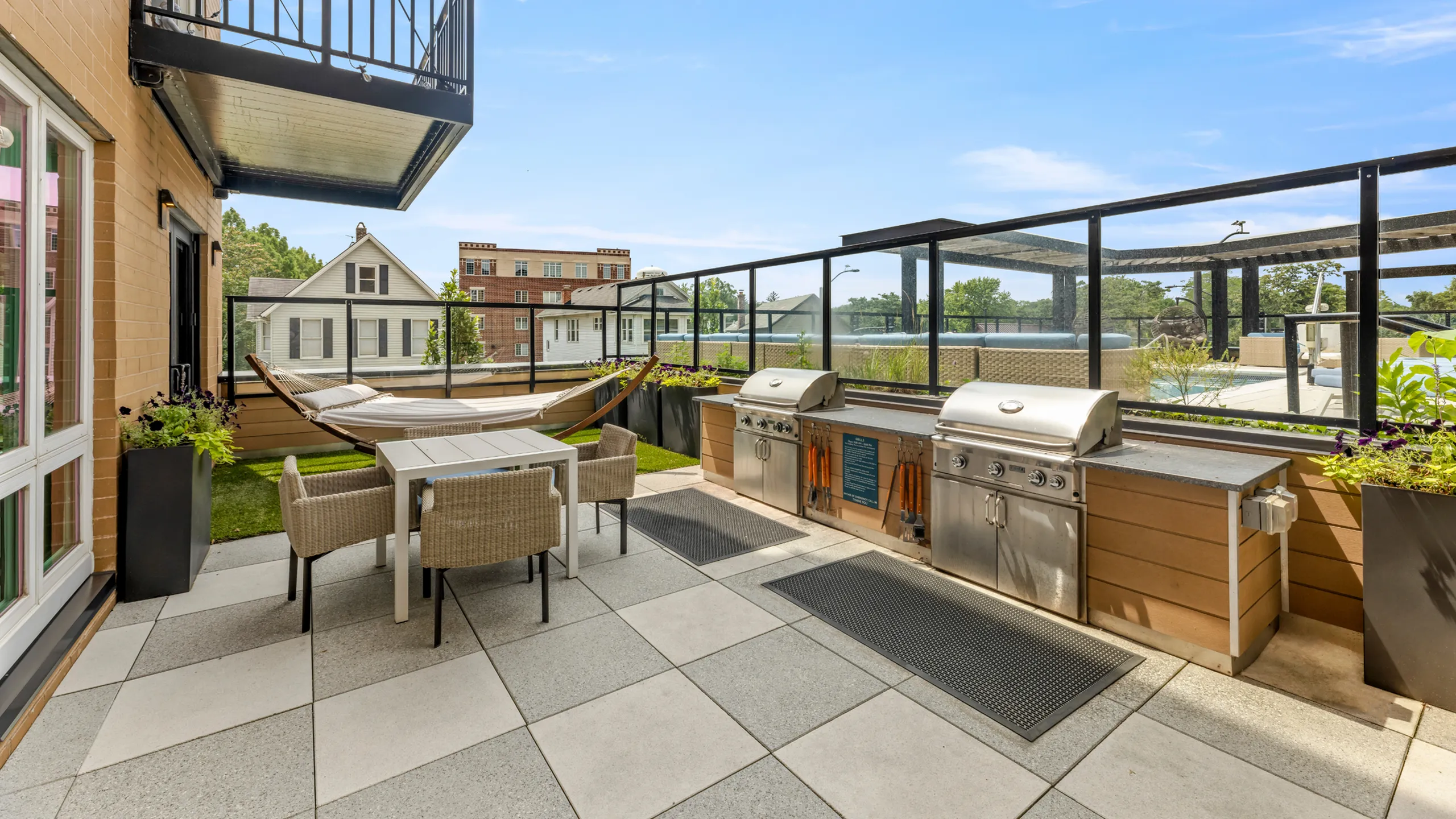 Luxurious apartment terrace featuring chic outdoor seating, modern grills, and a relaxing hammock with poolside views.