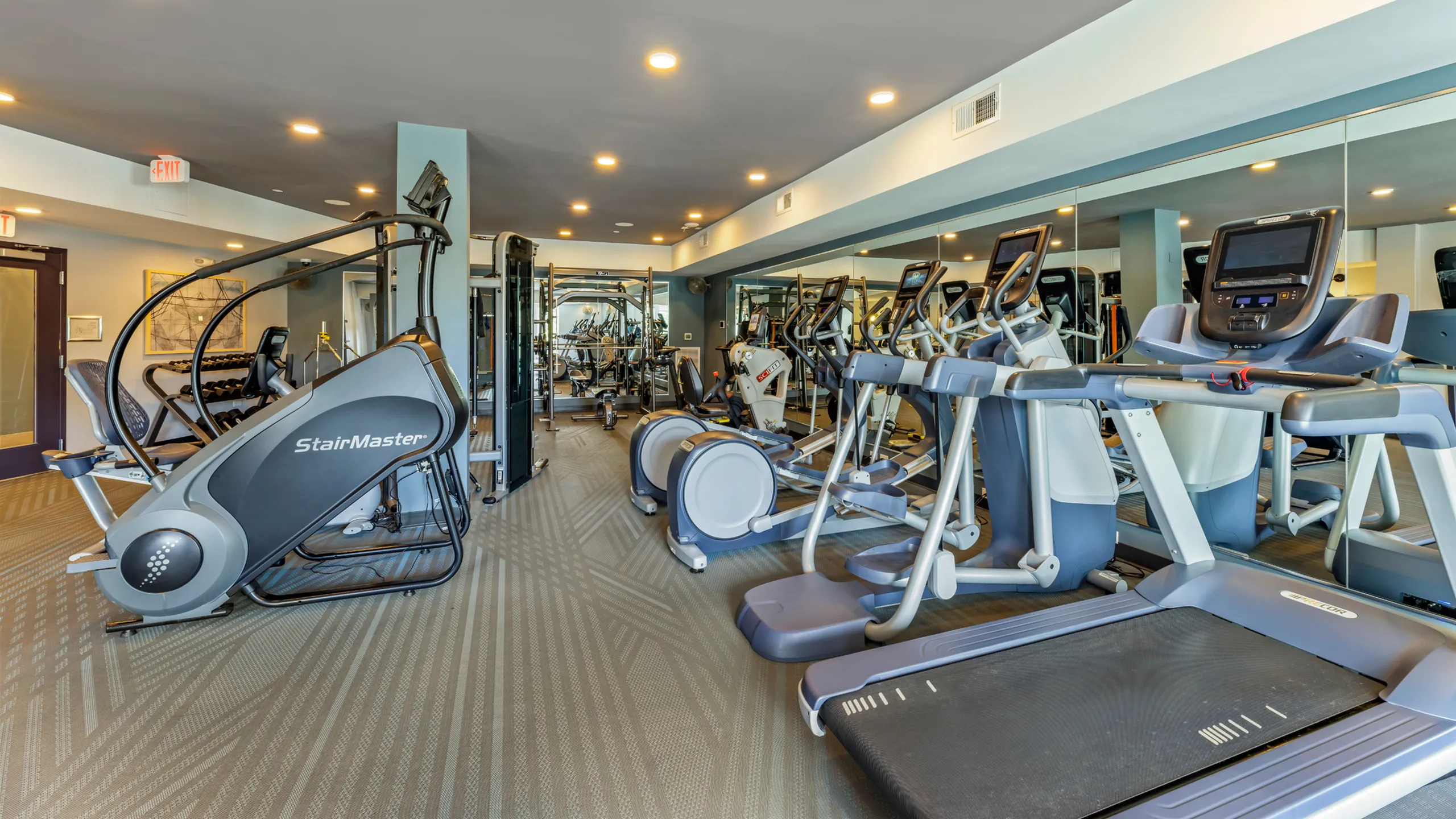Modern fitness center with state-of-the-art exercise equipment, including elliptical machines, treadmills, and a StairMaster, set in a spacious and well-lit environment.