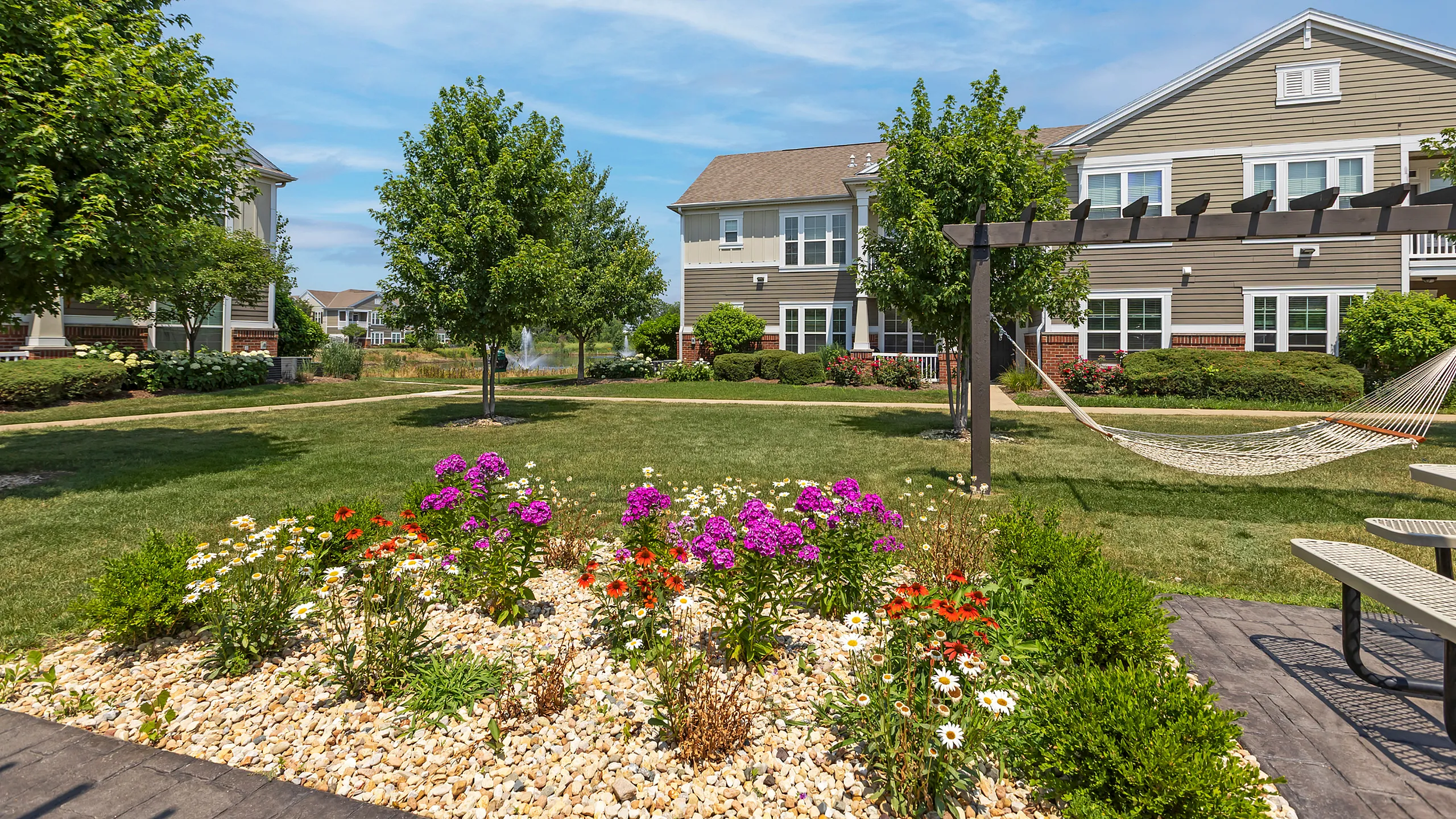 Charming residential complex with lush landscaping, vibrant flower garden, and a relaxing hammock under a pergola.