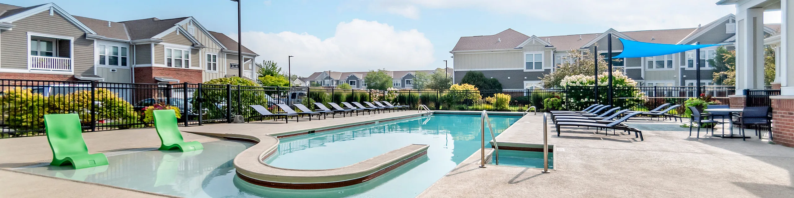 Inviting apartment complex exterior featuring a sparkling pool with stylish lounge chairs and lush landscaping.