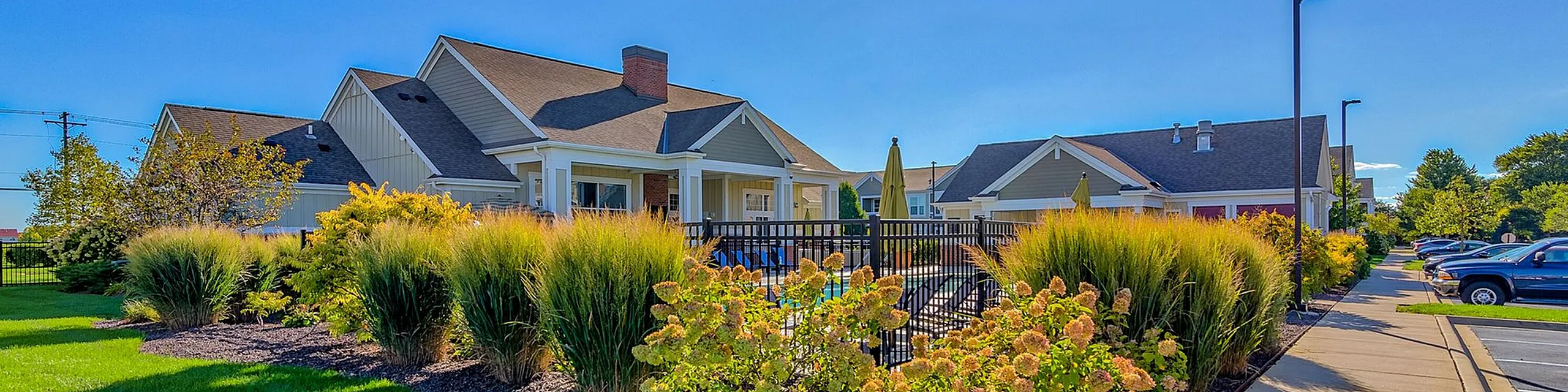 Charming residential community with lush landscaping, showcasing modern single-family homes under a clear blue sky.