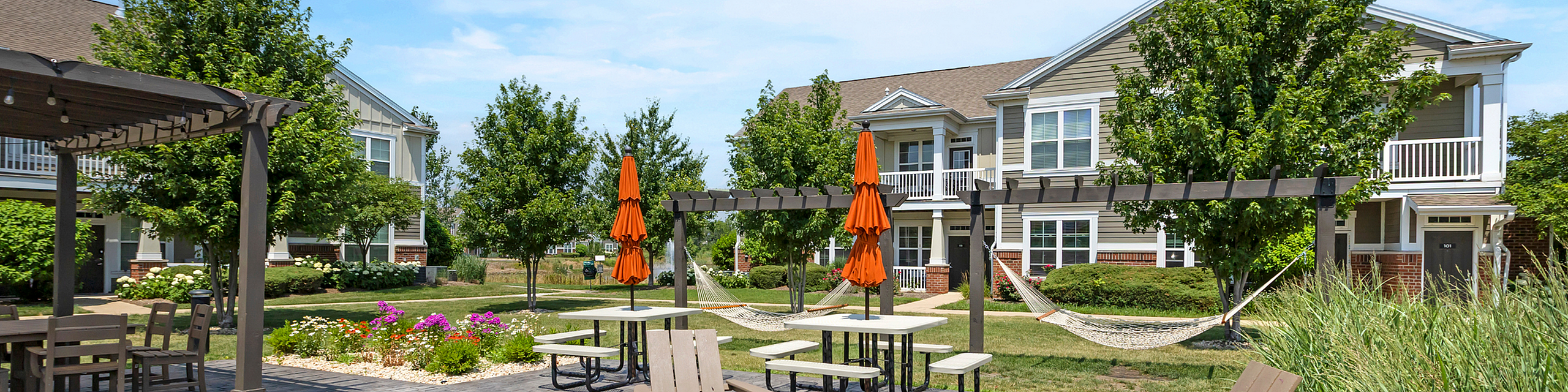 Charming apartment community with lush landscaping, outdoor seating, and inviting hammocks under a pergola, perfect for relaxation and social gatherings.