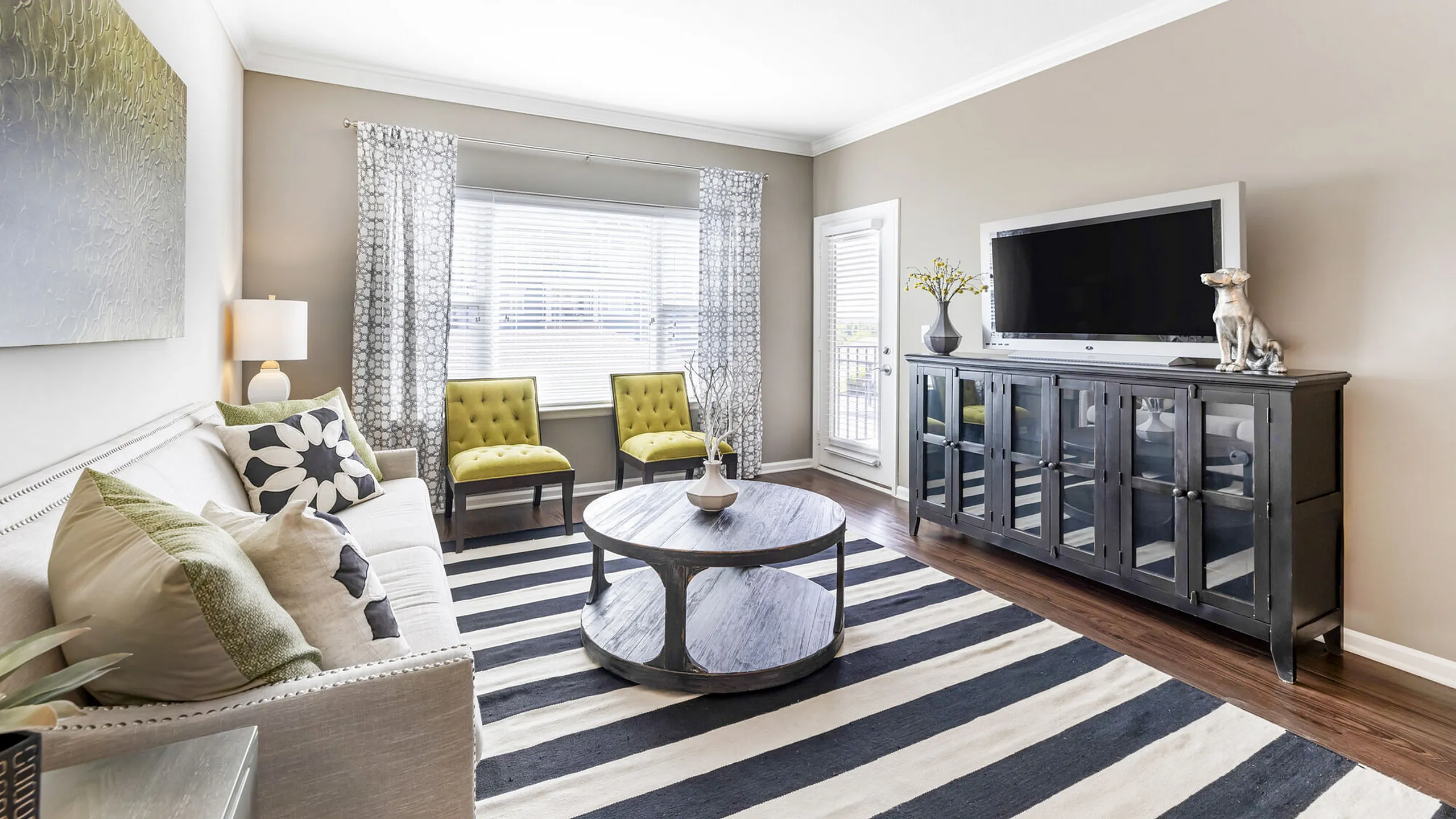Bright and inviting living room featuring chic decor, large windows, and a stylish round coffee table on a bold striped rug.