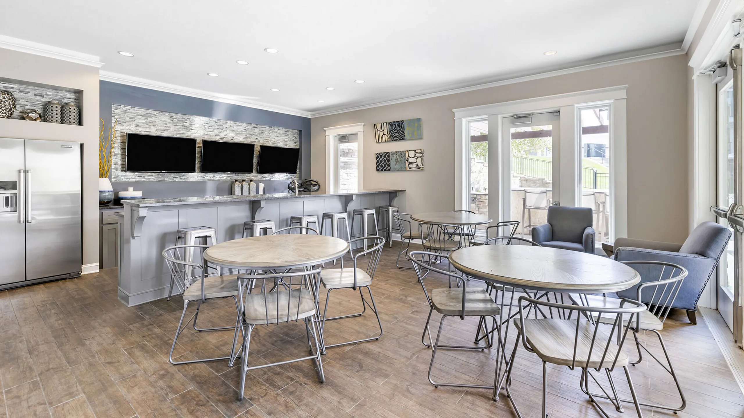 Bright and modern communal space featuring sleek bar seating, stylish round tables, and large windows offering natural light.