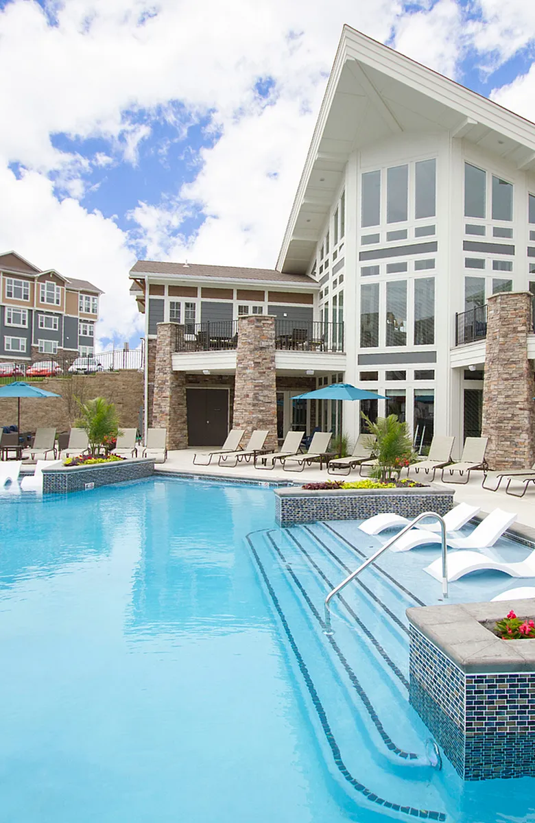 Luxurious apartment complex with a stunning outdoor pool, elegant poolside loungers, and impressive modern architecture.