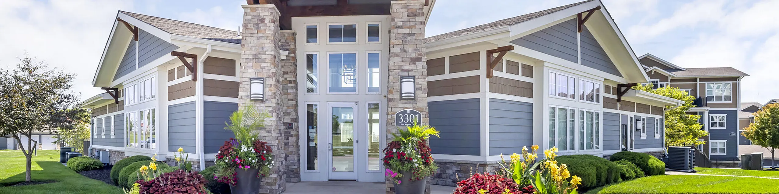 Charming apartment complex with stone accents, lush greenery, and vibrant flower beds, offering a welcoming entrance.