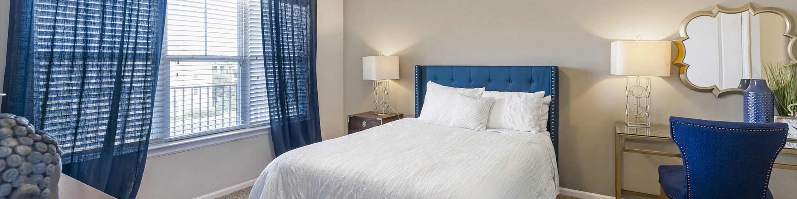 Elegant bedroom with a plush blue headboard, stylish decor, and ample natural light streaming through large windows.