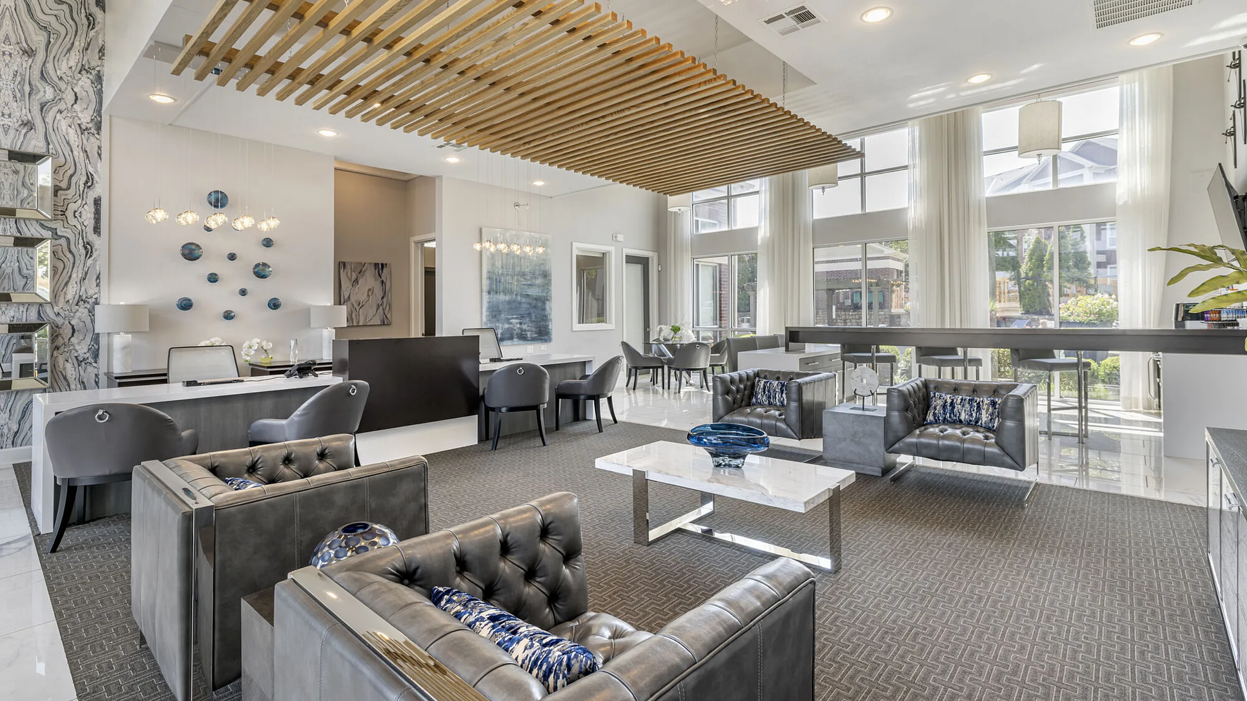 Elegant apartment lobby featuring modern decor with plush seating, stylish artwork, and expansive windows allowing natural light.