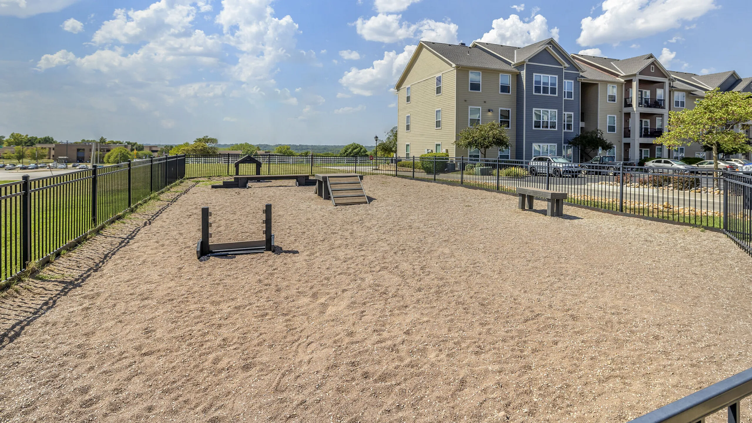 Charming apartment complex with a fenced pet-friendly outdoor play area, perfect for dog lovers, set against a backdrop of clear blue skies.