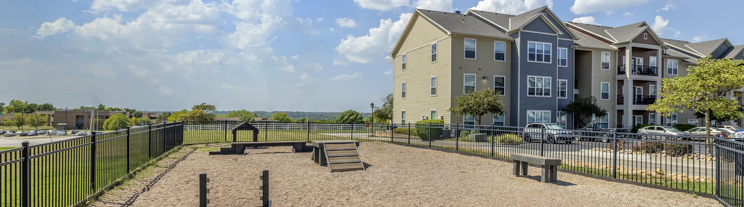 Sunny outdoor area with pet-friendly playground and modern apartment building, perfect for an active lifestyle.