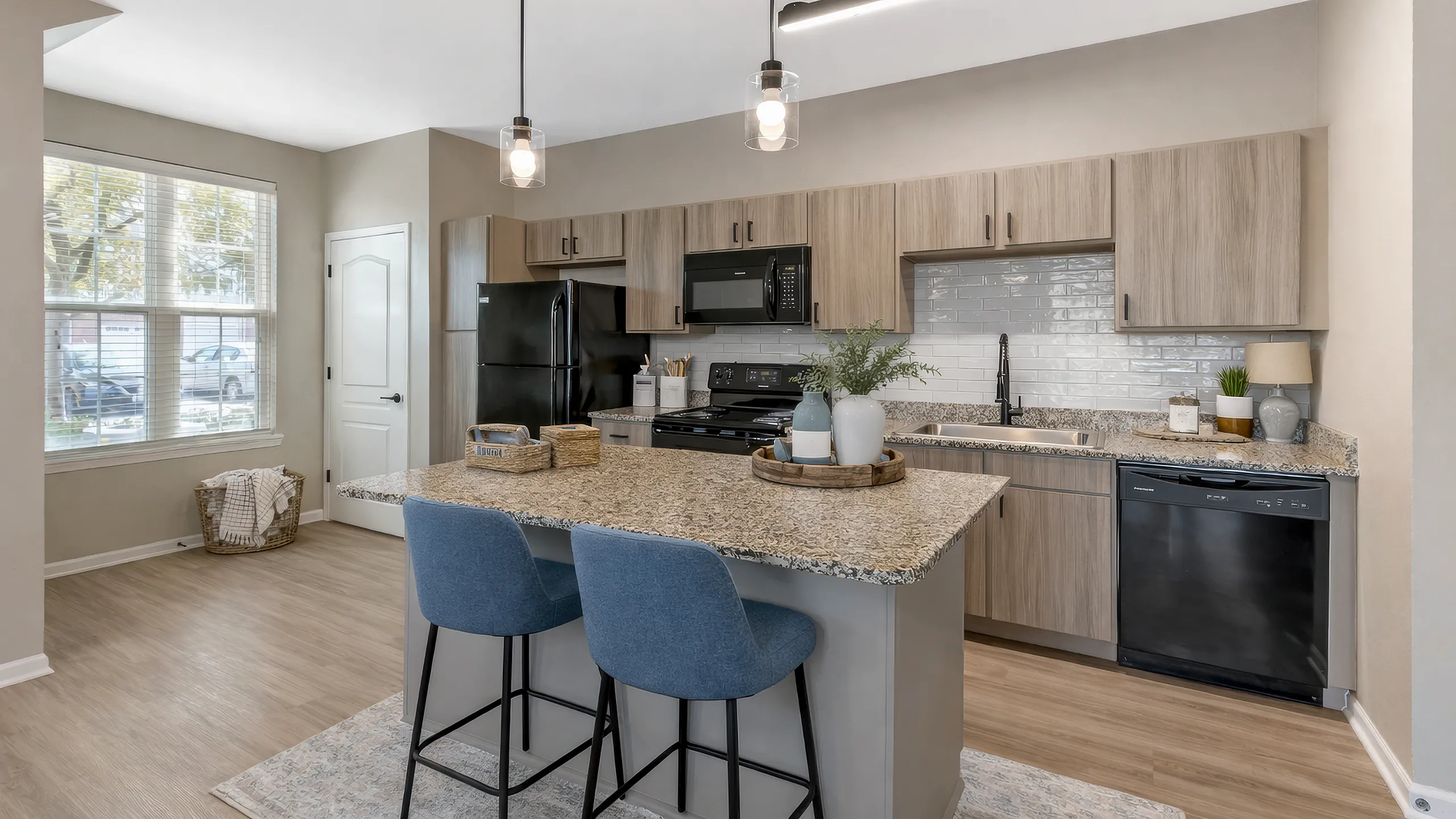 Modern kitchen with elegant granite countertops, chic pendant lighting, and stylish cabinetry, featuring an inviting breakfast bar with blue chairs.