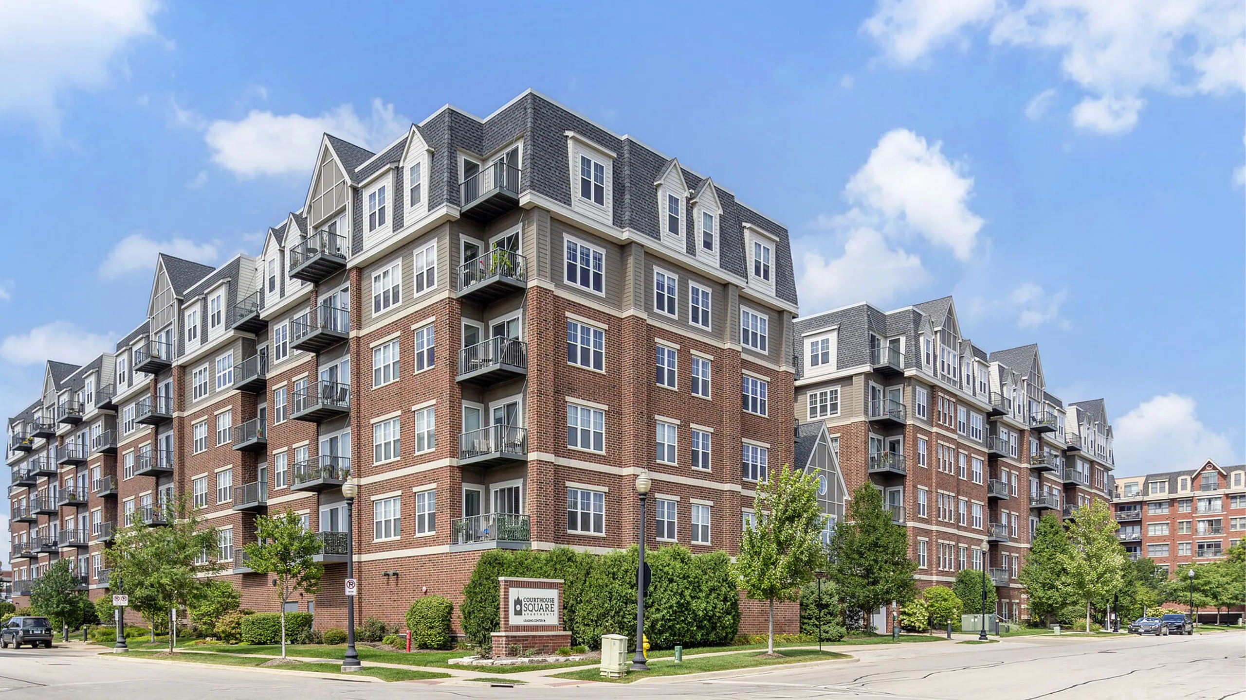 Charming urban apartment building with modern brick and gabled roofs, featuring private balconies and lush green surroundings.