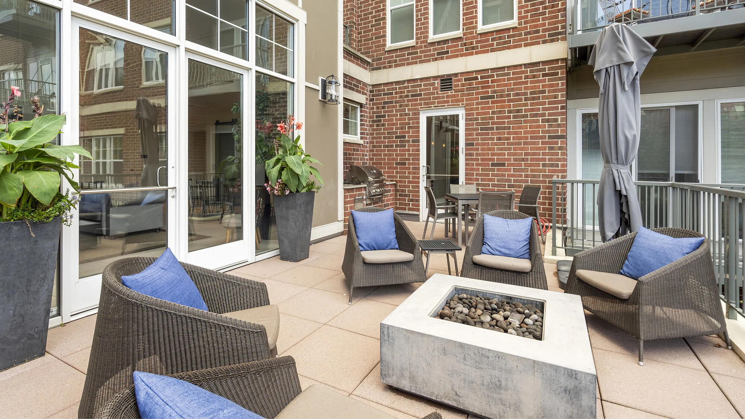 Chic outdoor patio with stylish wicker seating, cozy blue pillows, and a modern fire pit, ideal for relaxation and entertaining.
