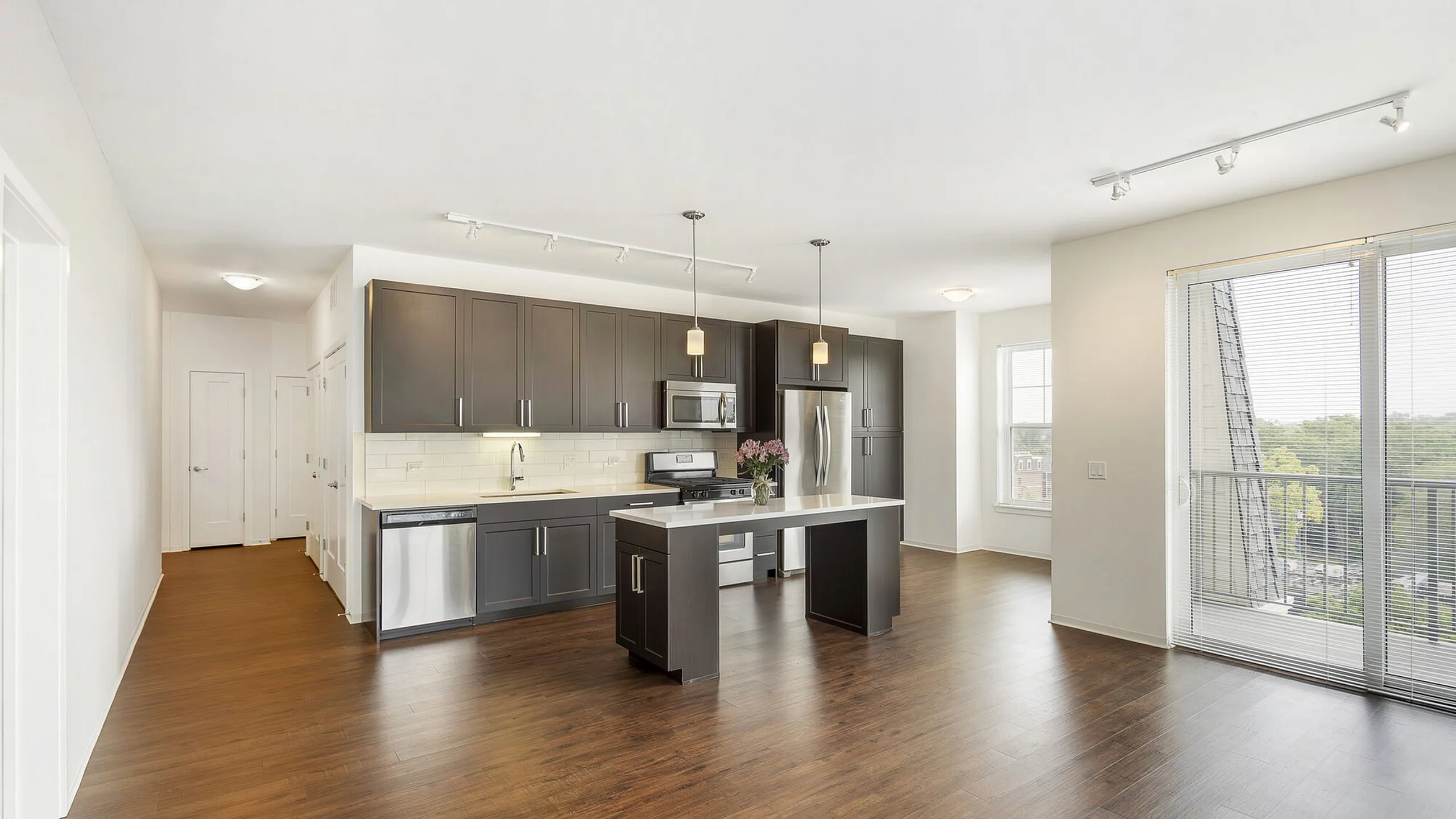 Modern kitchen with sleek dark cabinets, stainless steel appliances, and an inviting island, filled with natural light from large windows overlooking a lush view.