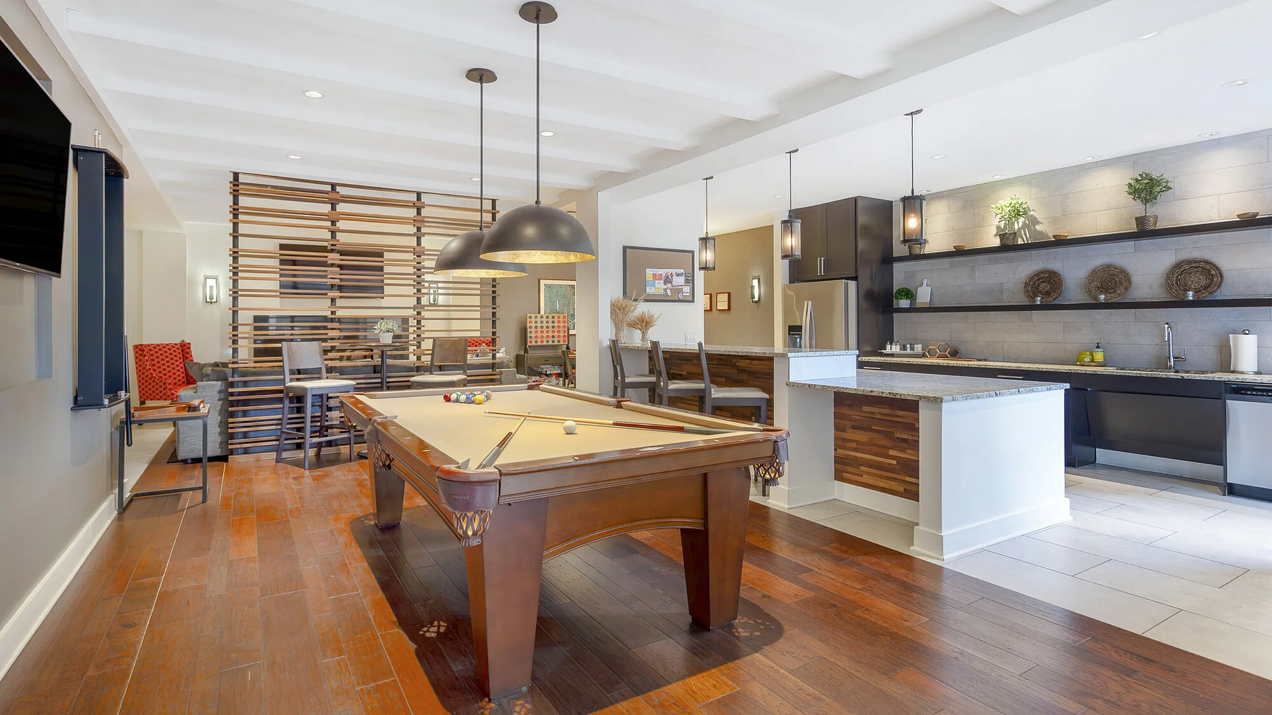 Elegant apartment interior with a modern kitchen, spacious island, and a stylish pool table, complemented by warm wooden flooring and chic pendant lighting.
