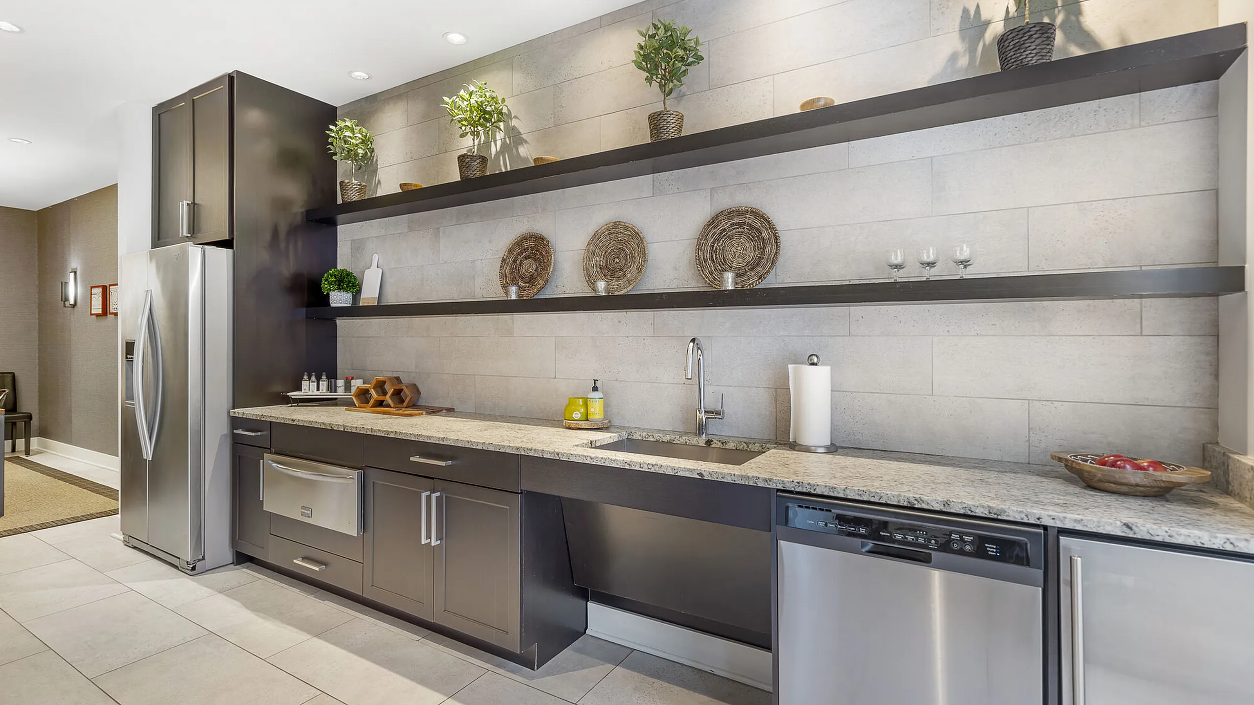Modern kitchen with sleek stainless steel appliances, elegant granite countertops, and stylish open shelving adorned with decorative plants and baskets.