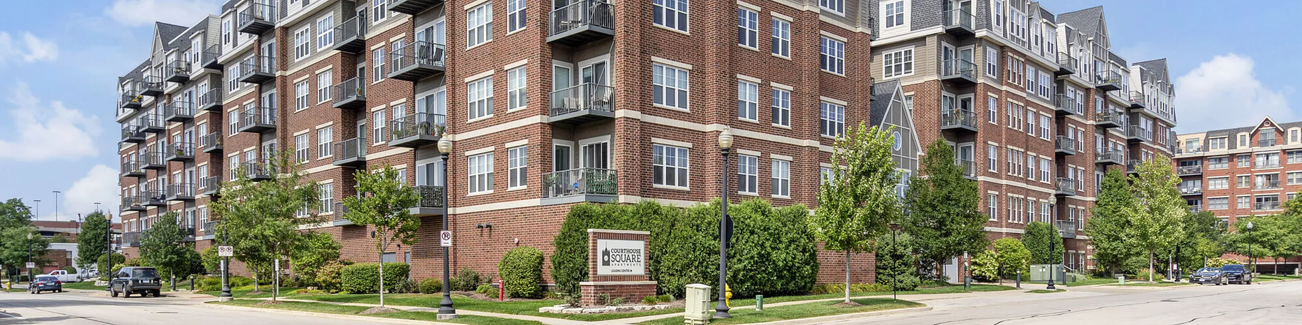 Elegant brick apartment building with multiple balconies, lush landscaping, and convenient urban setting.